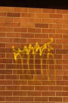 Yellow graffiti spray painted on a brick wall.