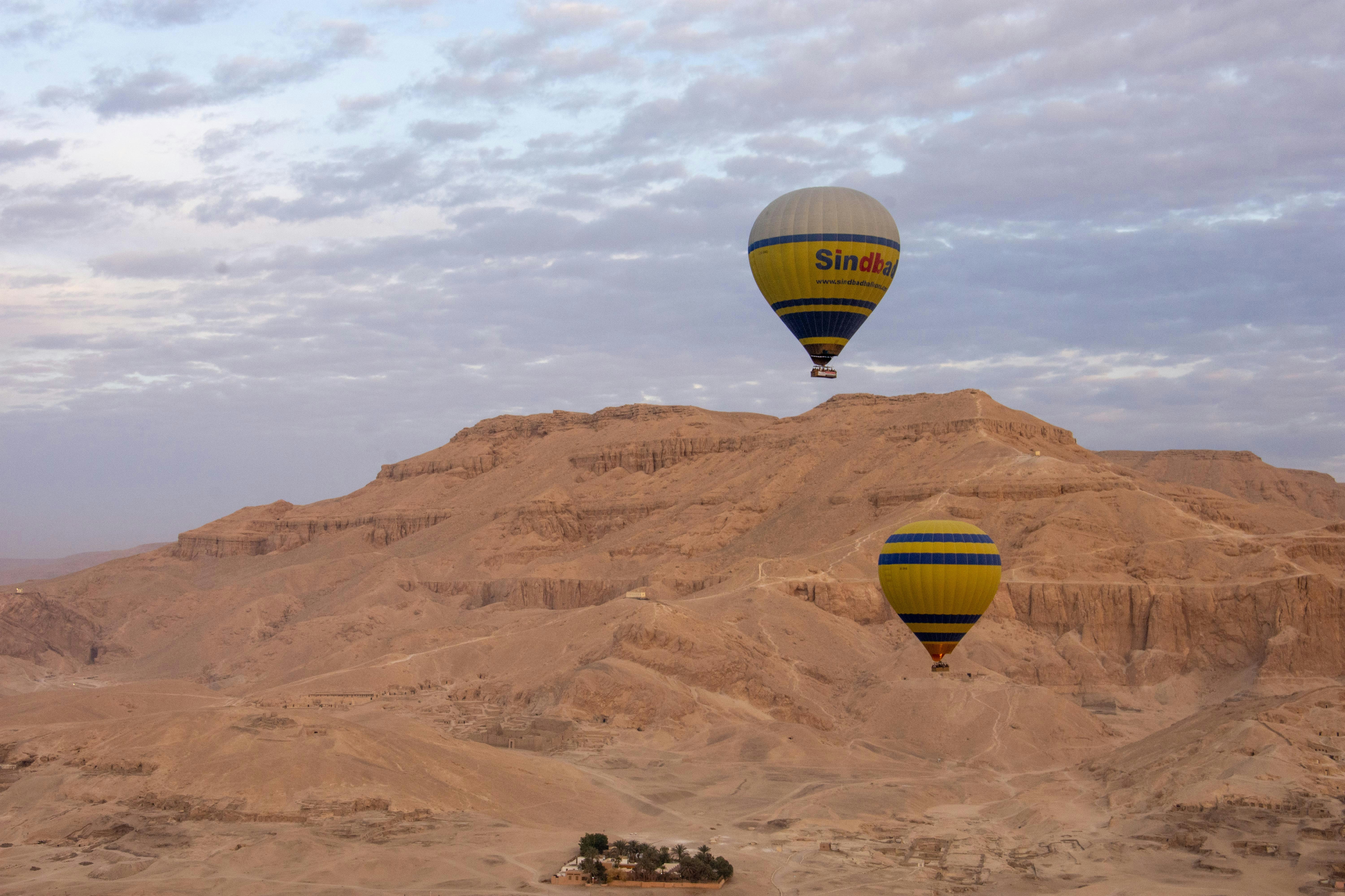 Two hot air balloons fly over desert mountains.