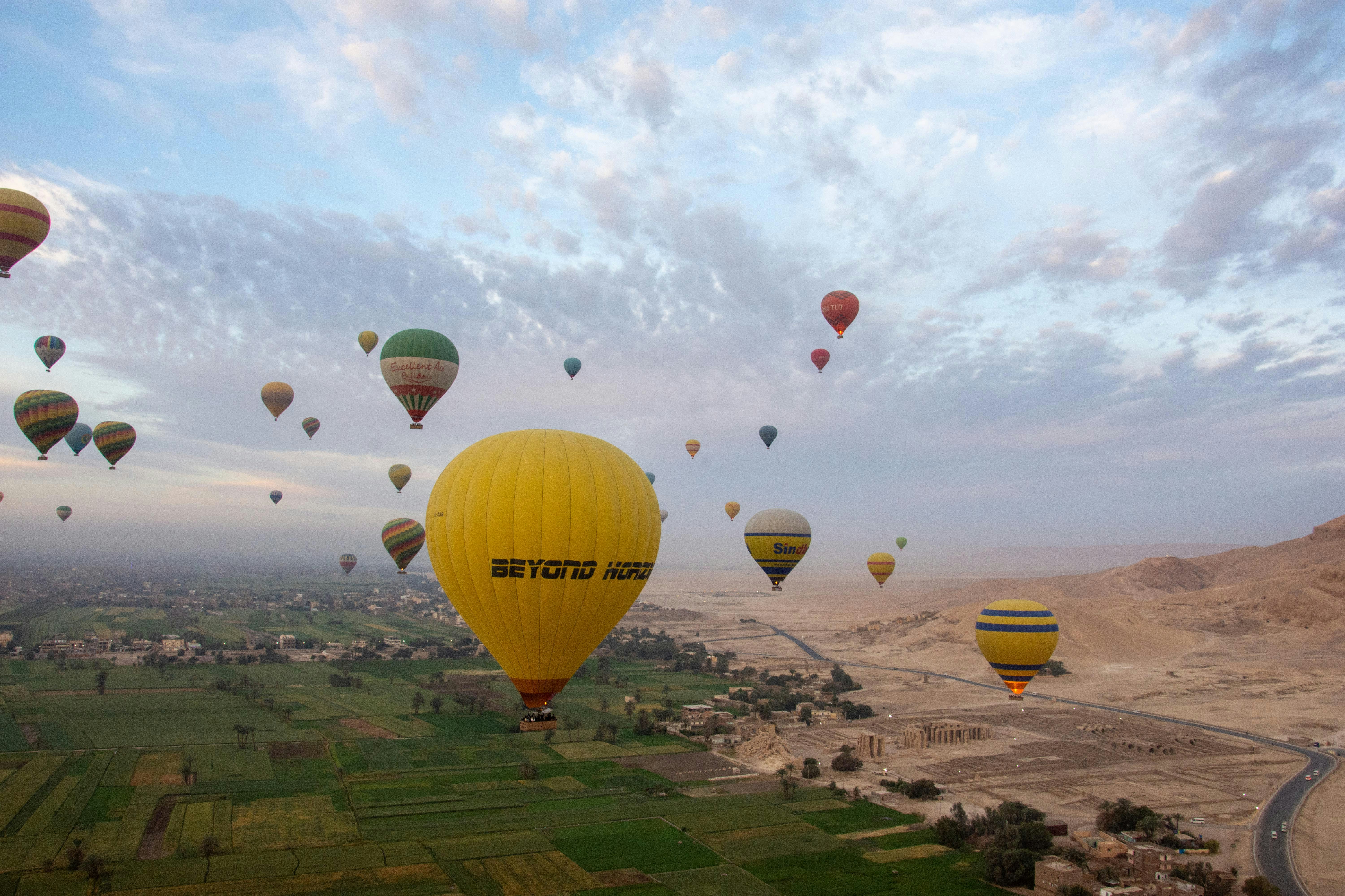 Many hot air balloons fly over a green valley.