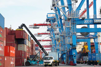Container ship loading with cranes and forklift at port.