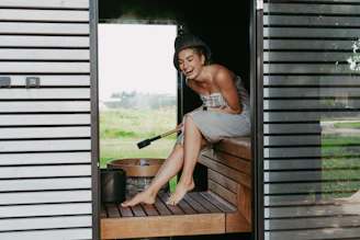 Woman laughing in a steamy sauna with a whisk