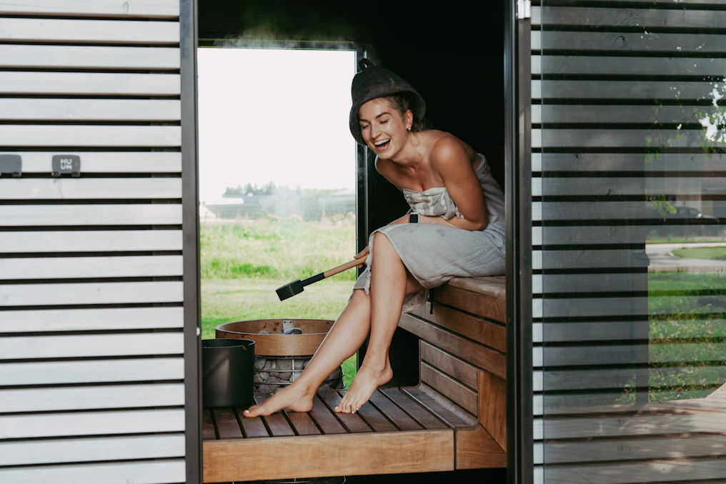 Woman laughing in a steamy sauna with a whisk