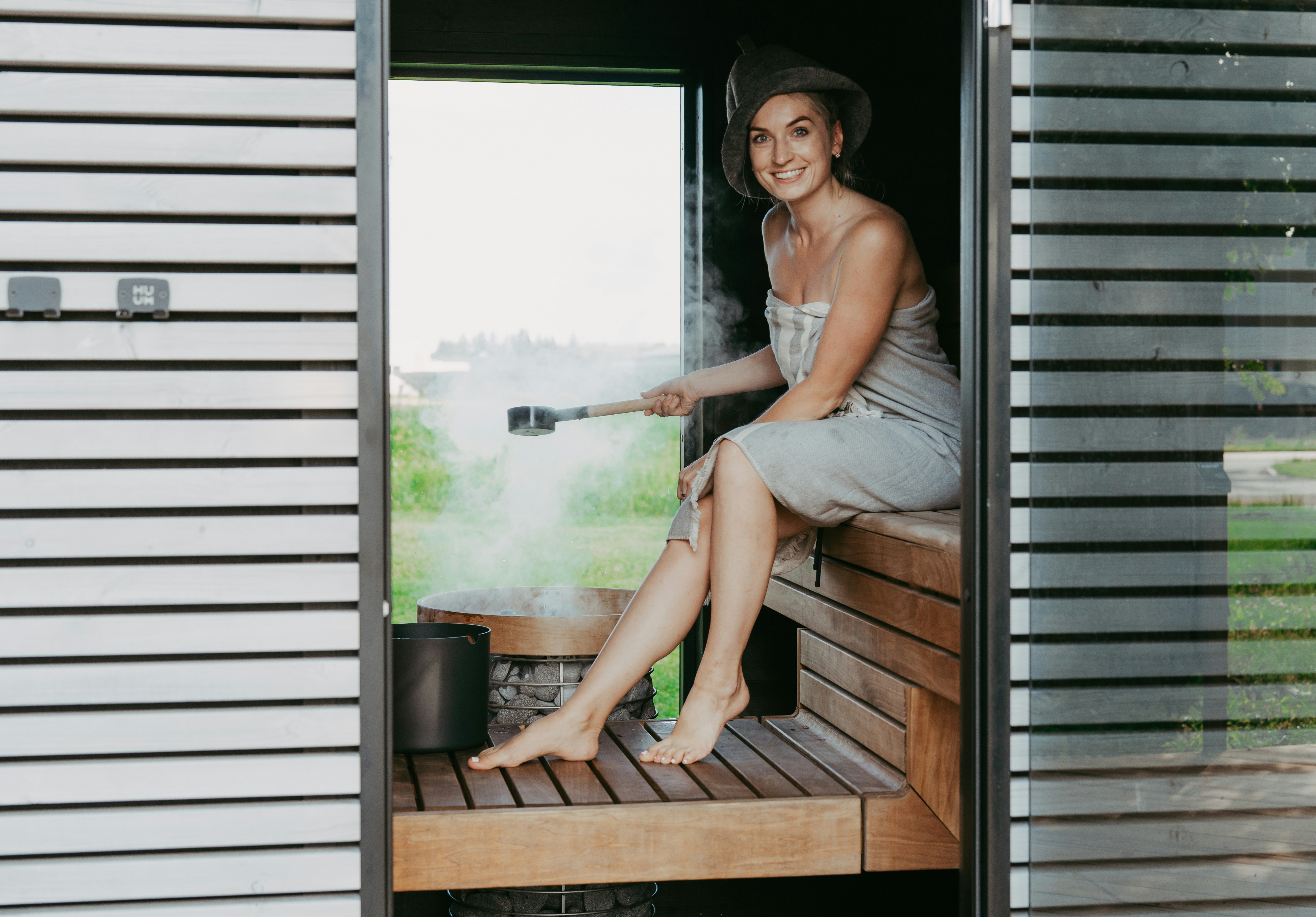 Woman in sauna pouring water on hot stones