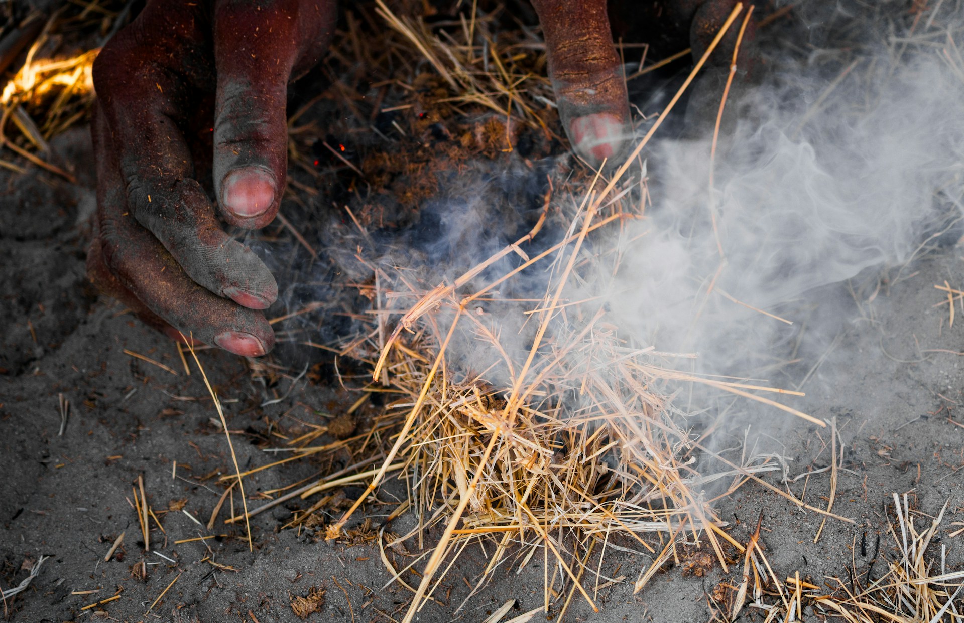 Hands making fire with dry grass and smoke