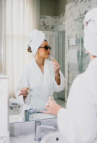 Woman in bathrobe applies lipstick in mirror