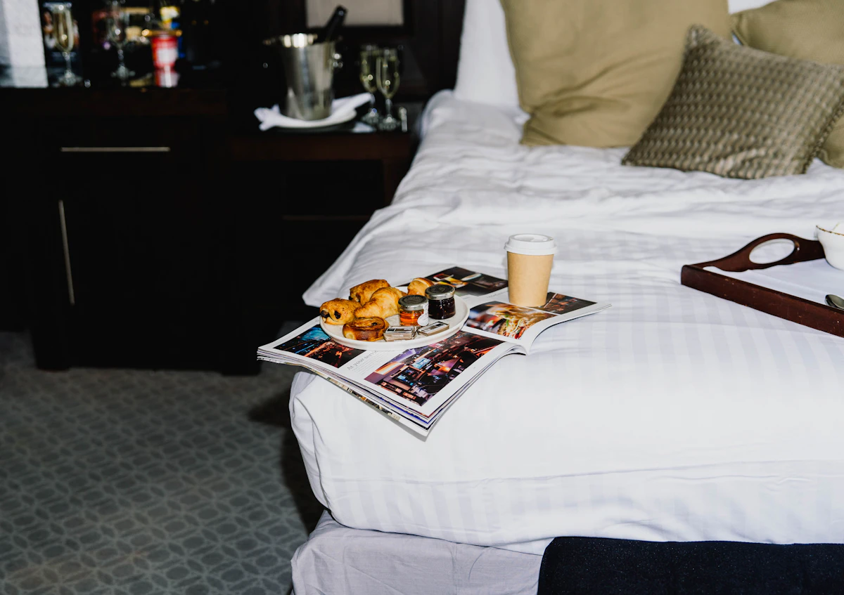 Breakfast tray with croissants and coffee on bed.