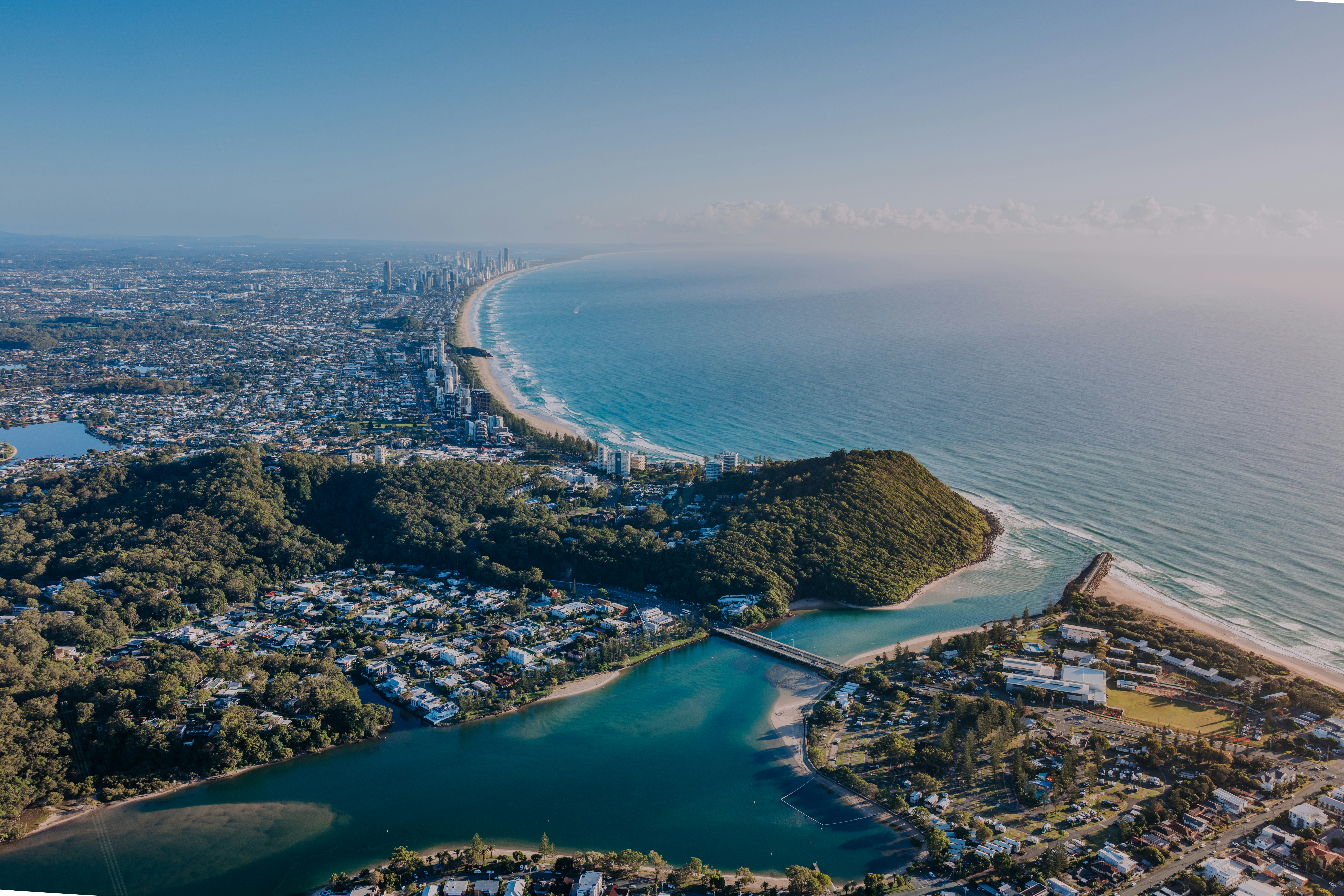 Coastal city with ocean, river, and green hills.