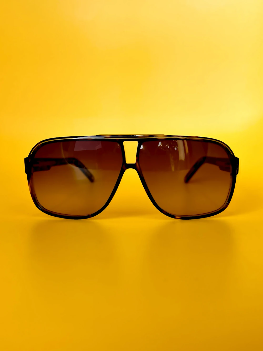 Oversized tortoise aviator sunglasses with amber gradient lenses on a saturated yellow background