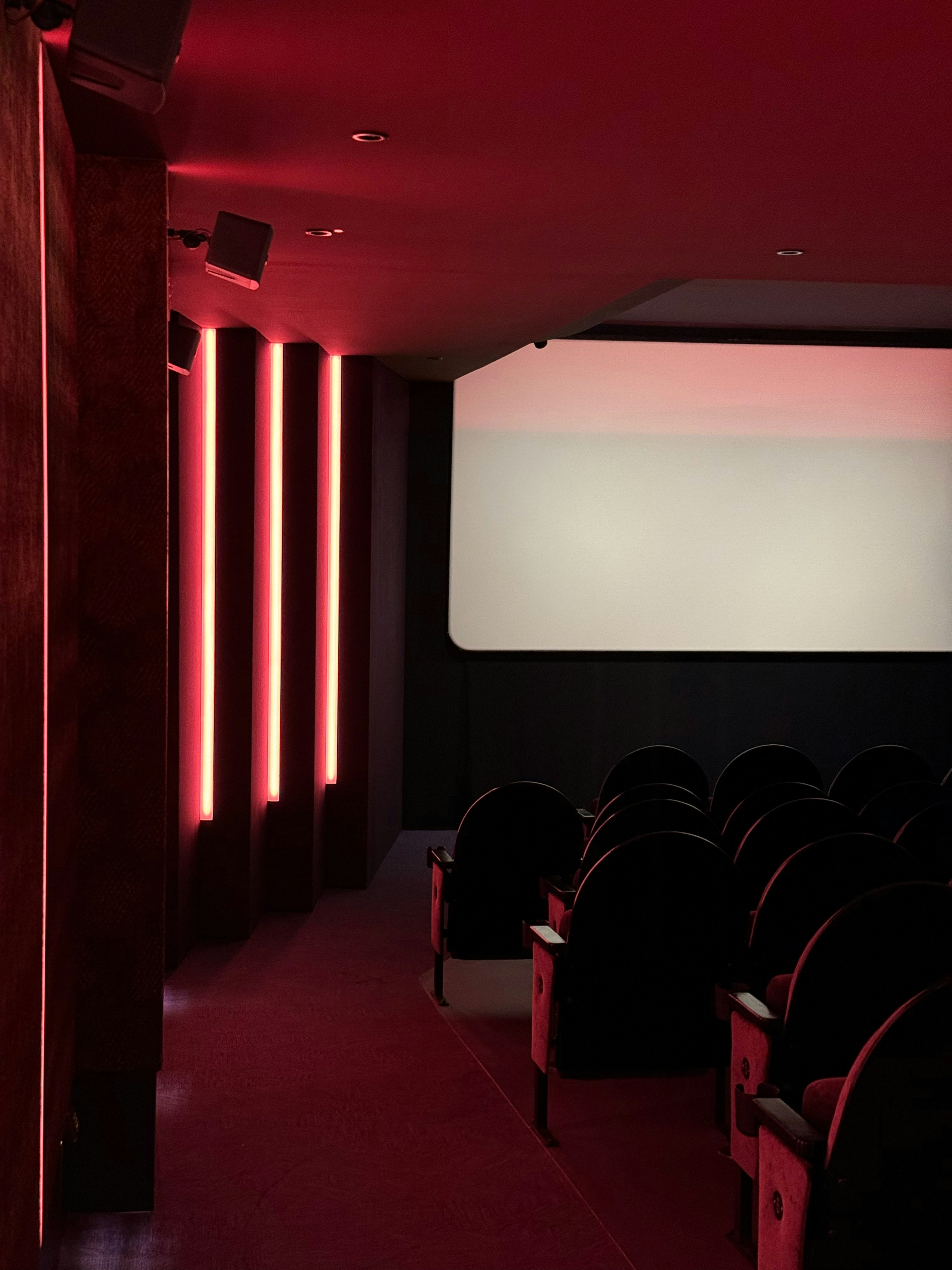 Empty cinema hall with red lighting and seats.