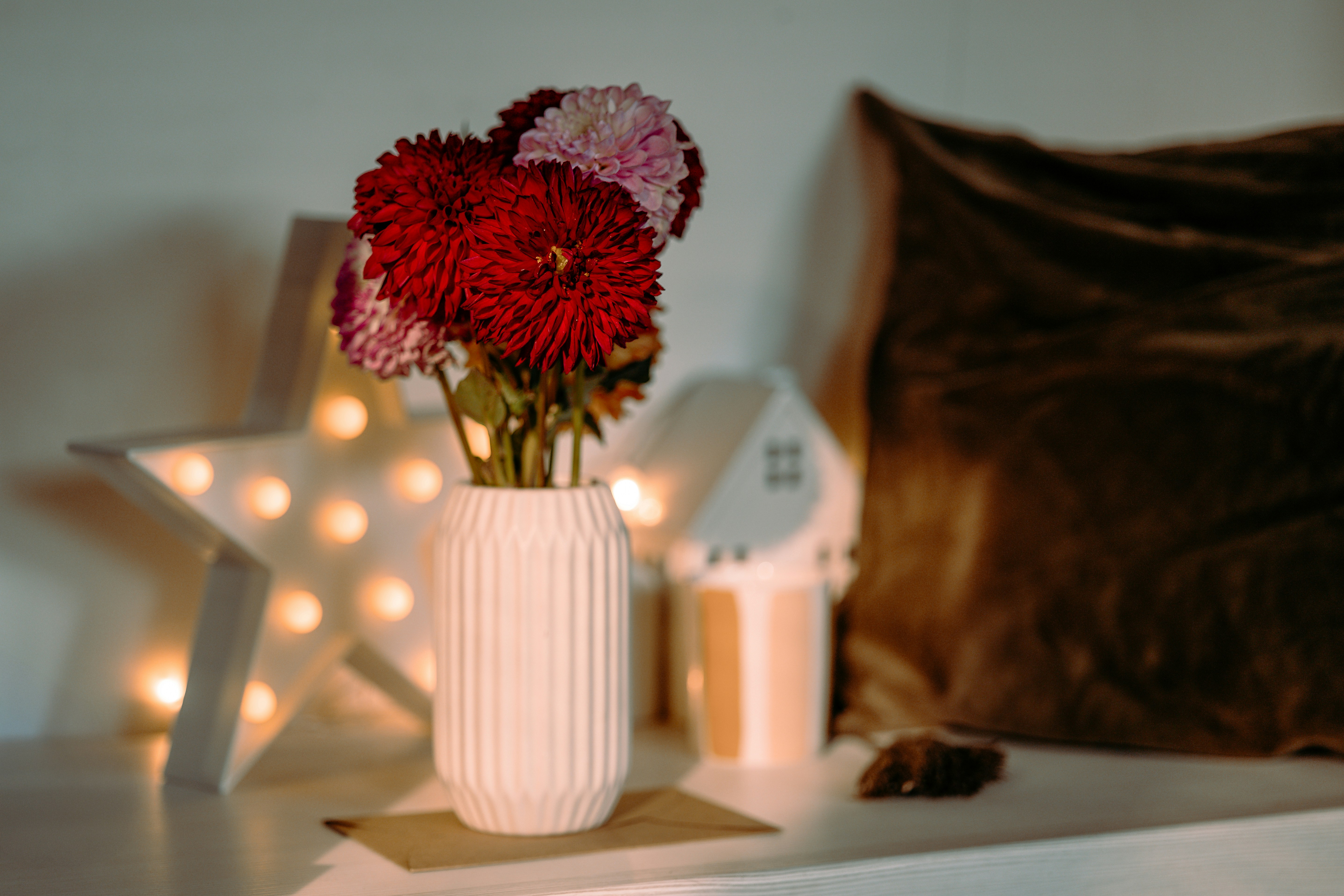 White vase with red and pink flowers on shelf.