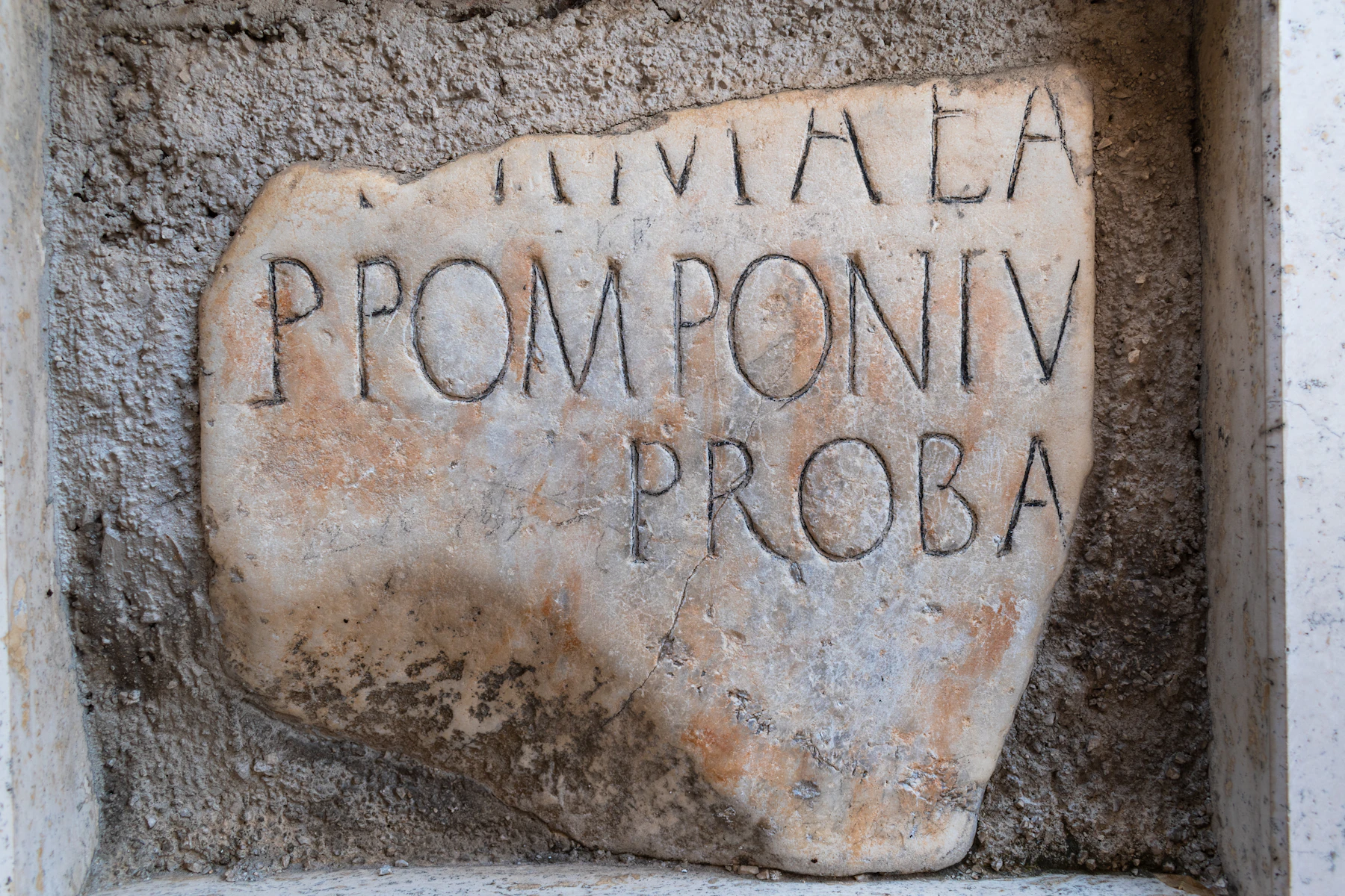 A broken piece of marble carved with part of a Roman name, mortared into a wall niche