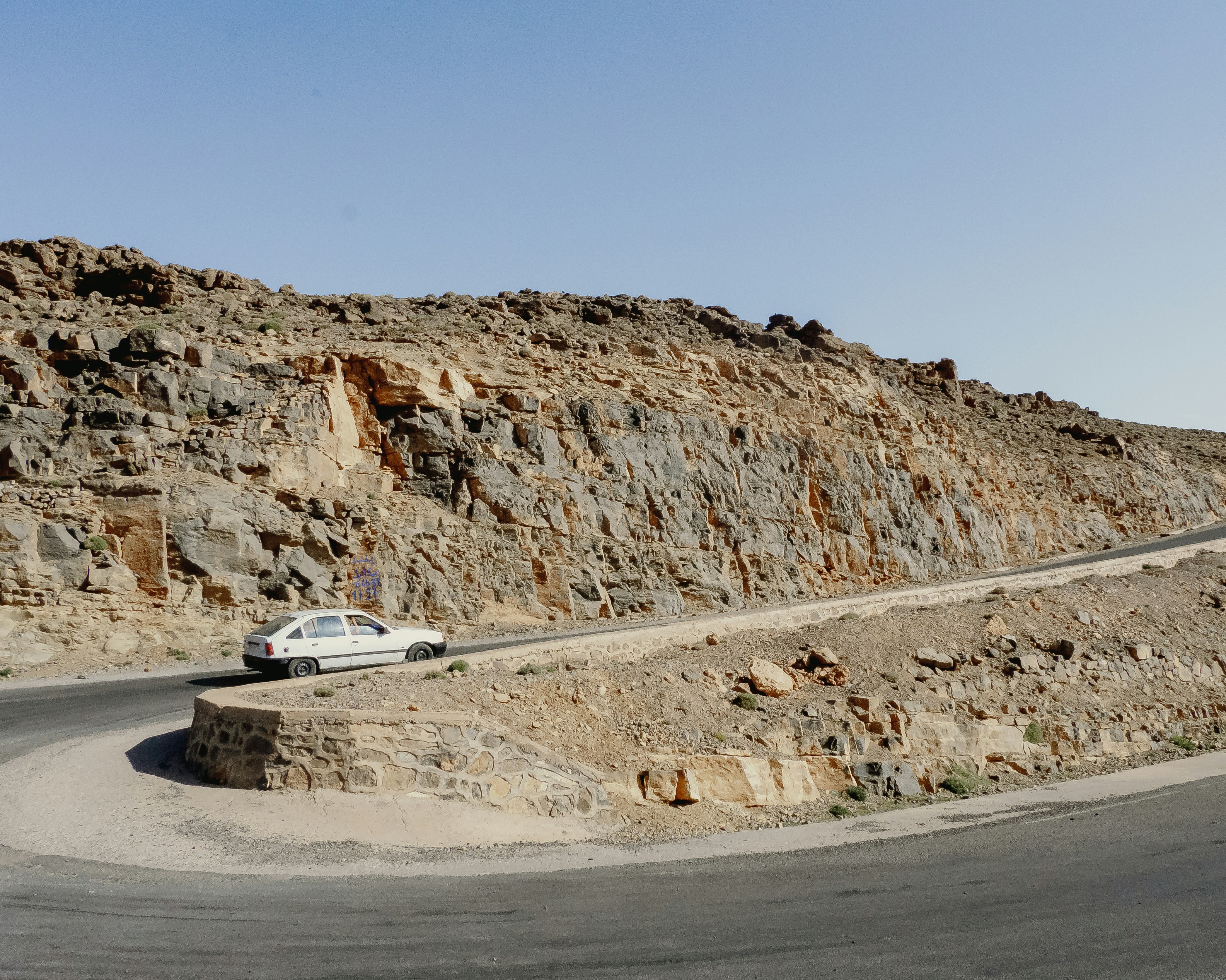 Weißes Auto, das auf einer kurvenreichen Straße durch felsiges Gelände fährt.
