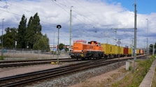 Orange locomotive pulls colorful cargo train on tracks.