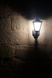 A vintage lantern illuminates a stone wall at night.