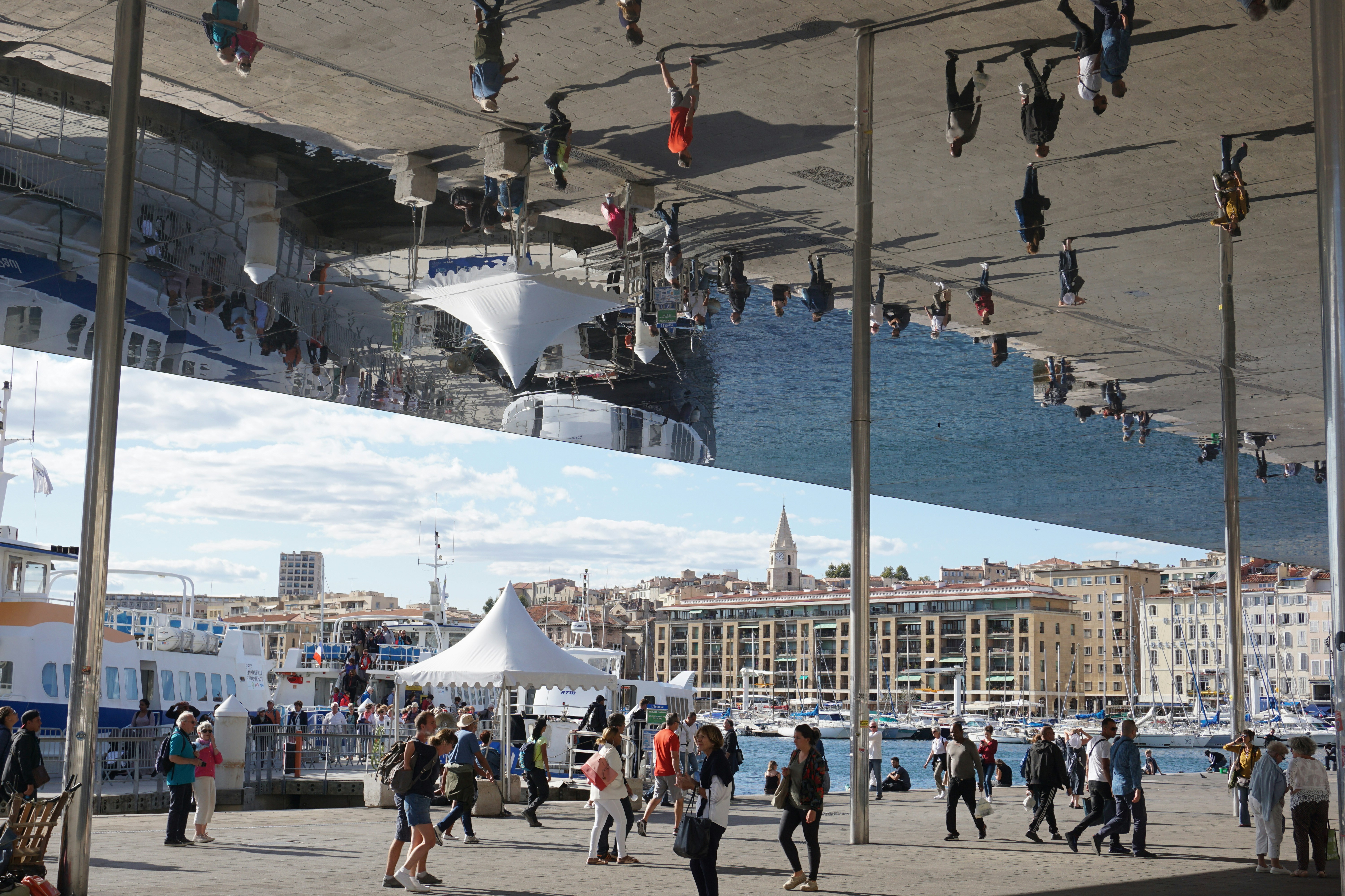 People walk under a mirrored ceiling reflecting the city