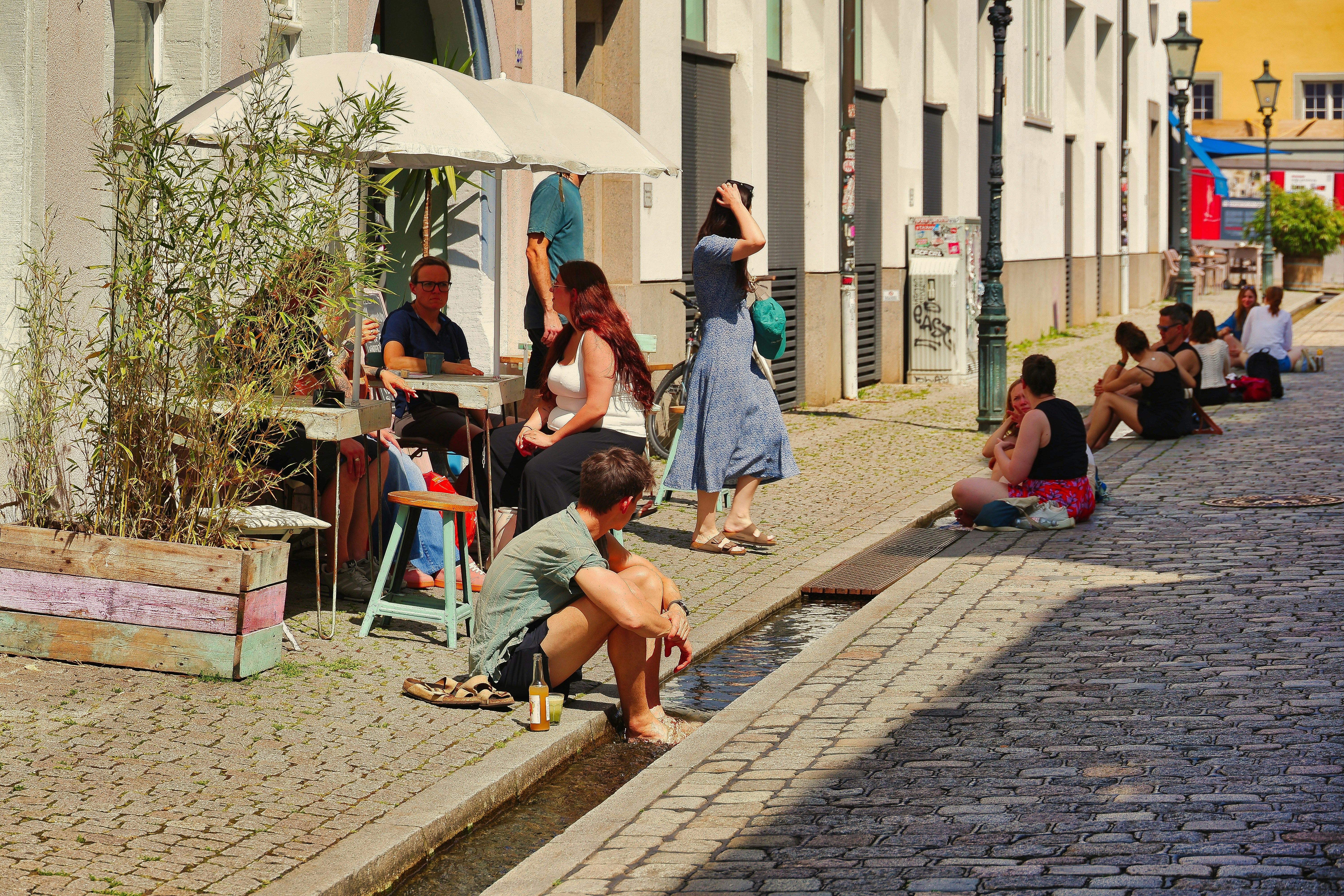 People relaxing on a sunny street next to a building.