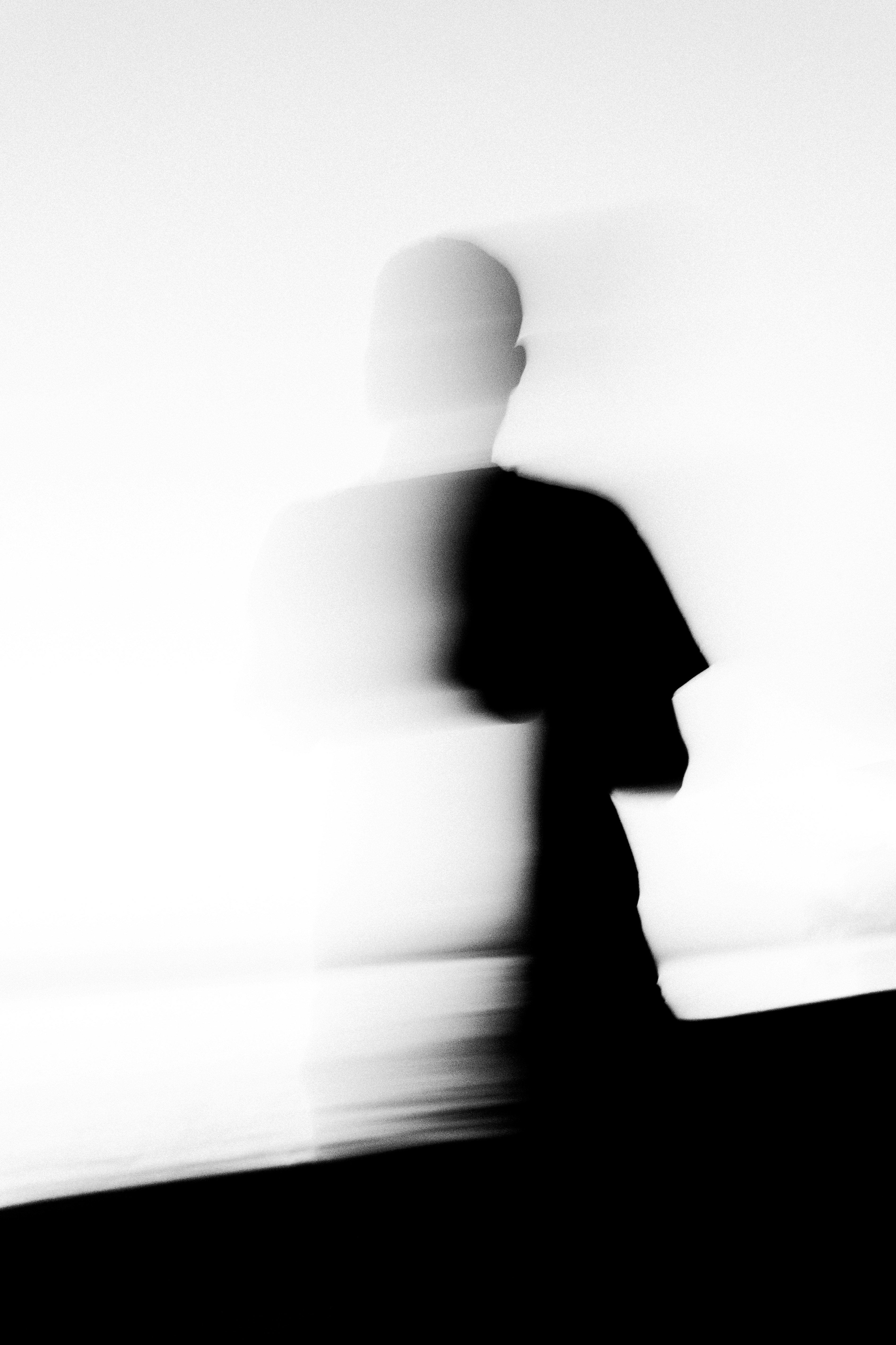 Blurred silhouette of a person walking against a bright background.