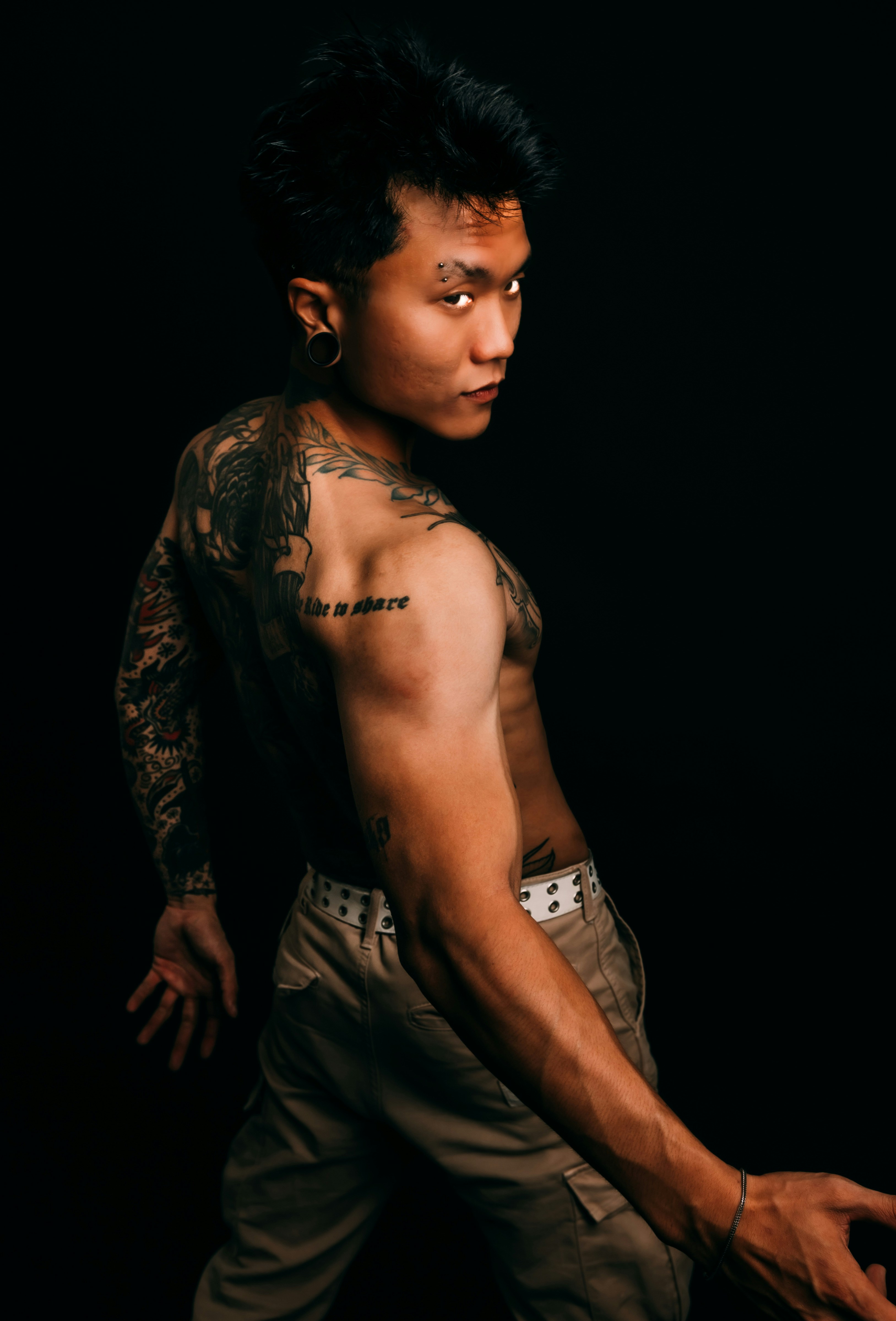 Homem tatuado olhando por cima do ombro contra fundo preto
