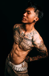 Man with extensive tattoos poses against black background