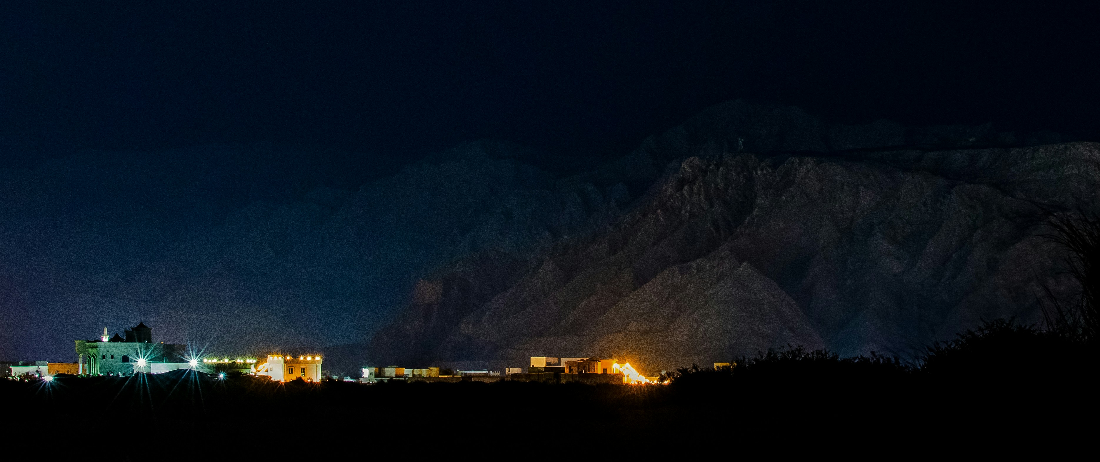 Illuminated buildings at the base of dark mountains at night