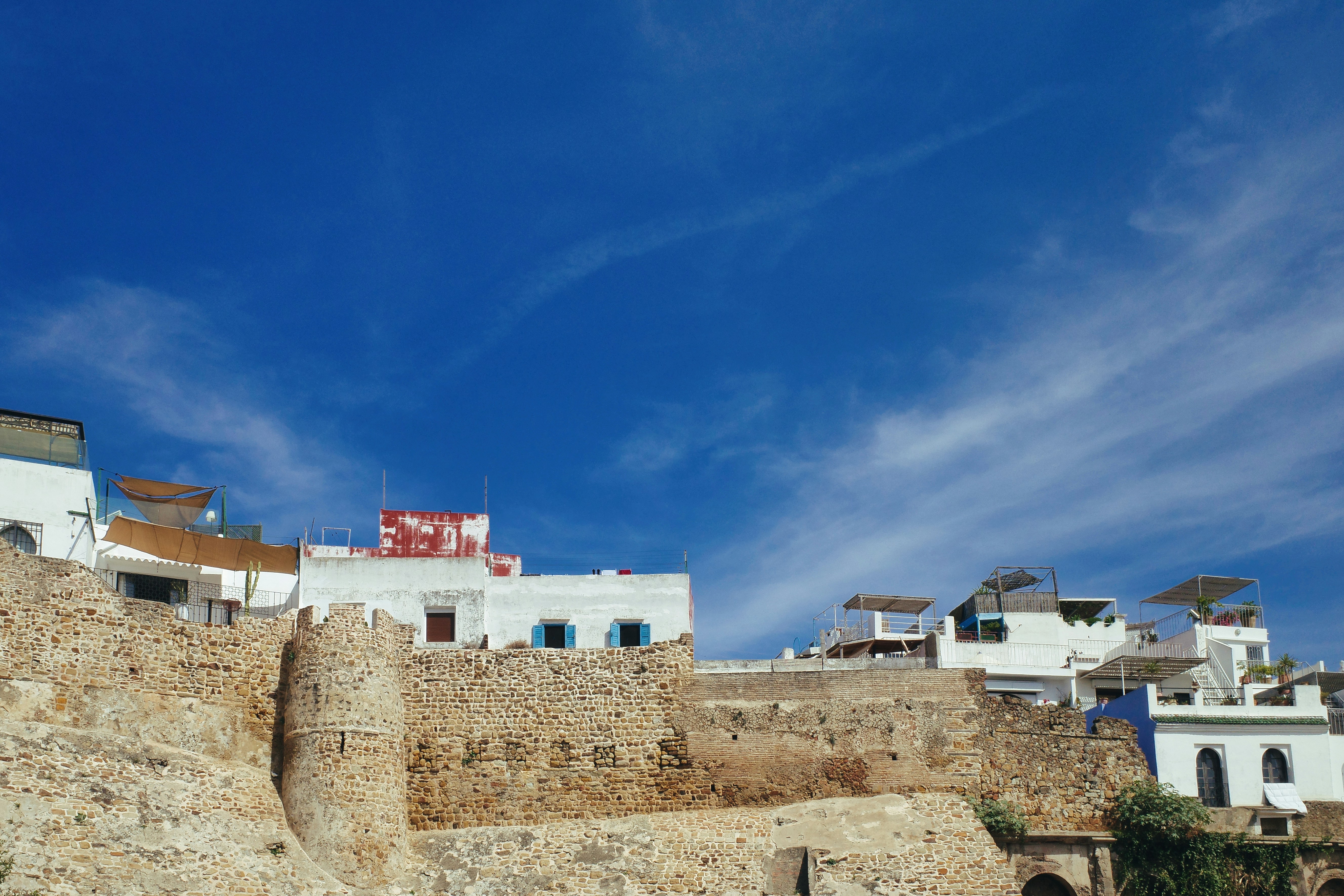 Des bâtiments blancs au sommet d’anciens murs de pierre sous un ciel bleu.