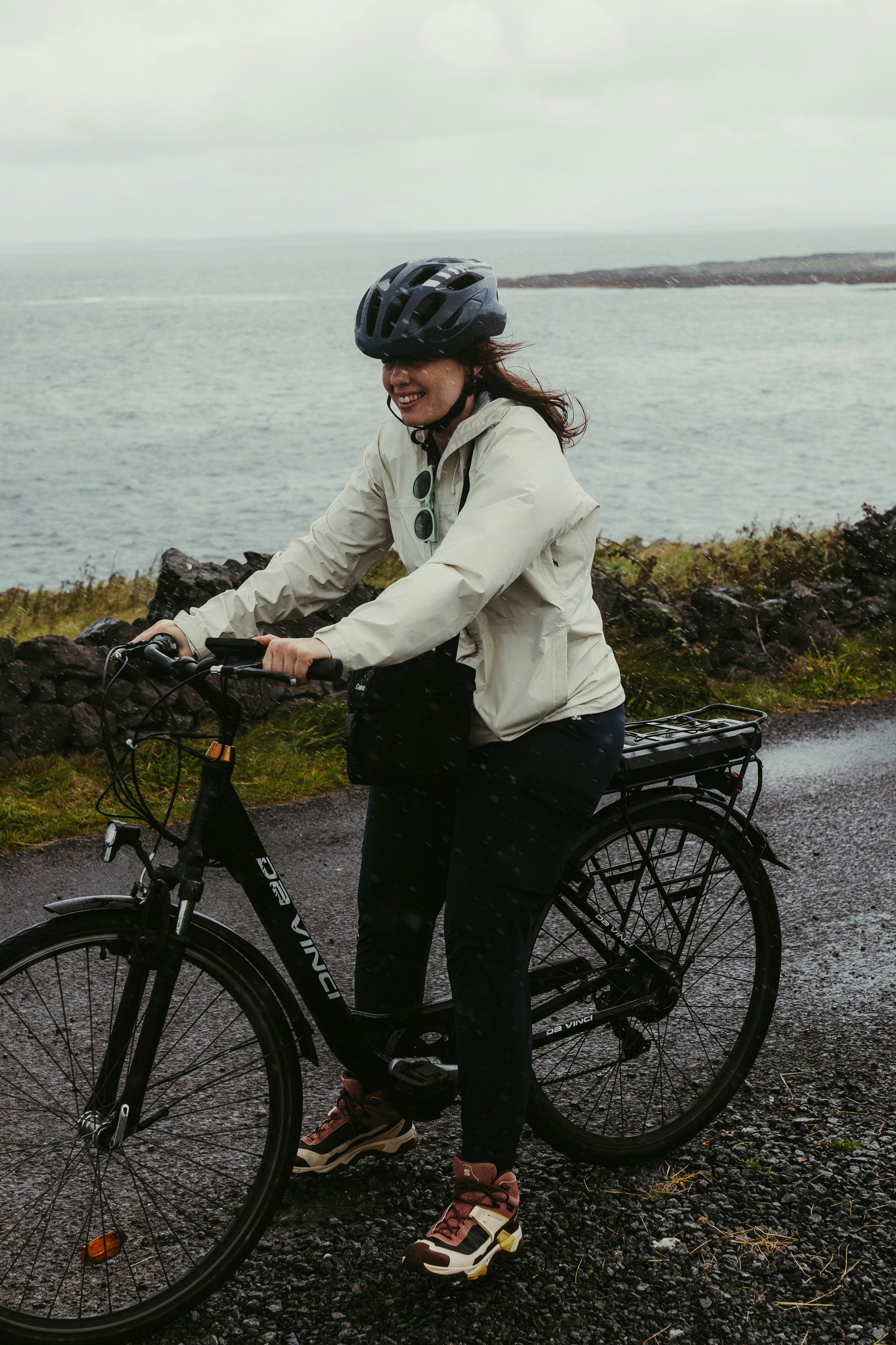 Woman in helmet riding a bicycle near the ocean.
