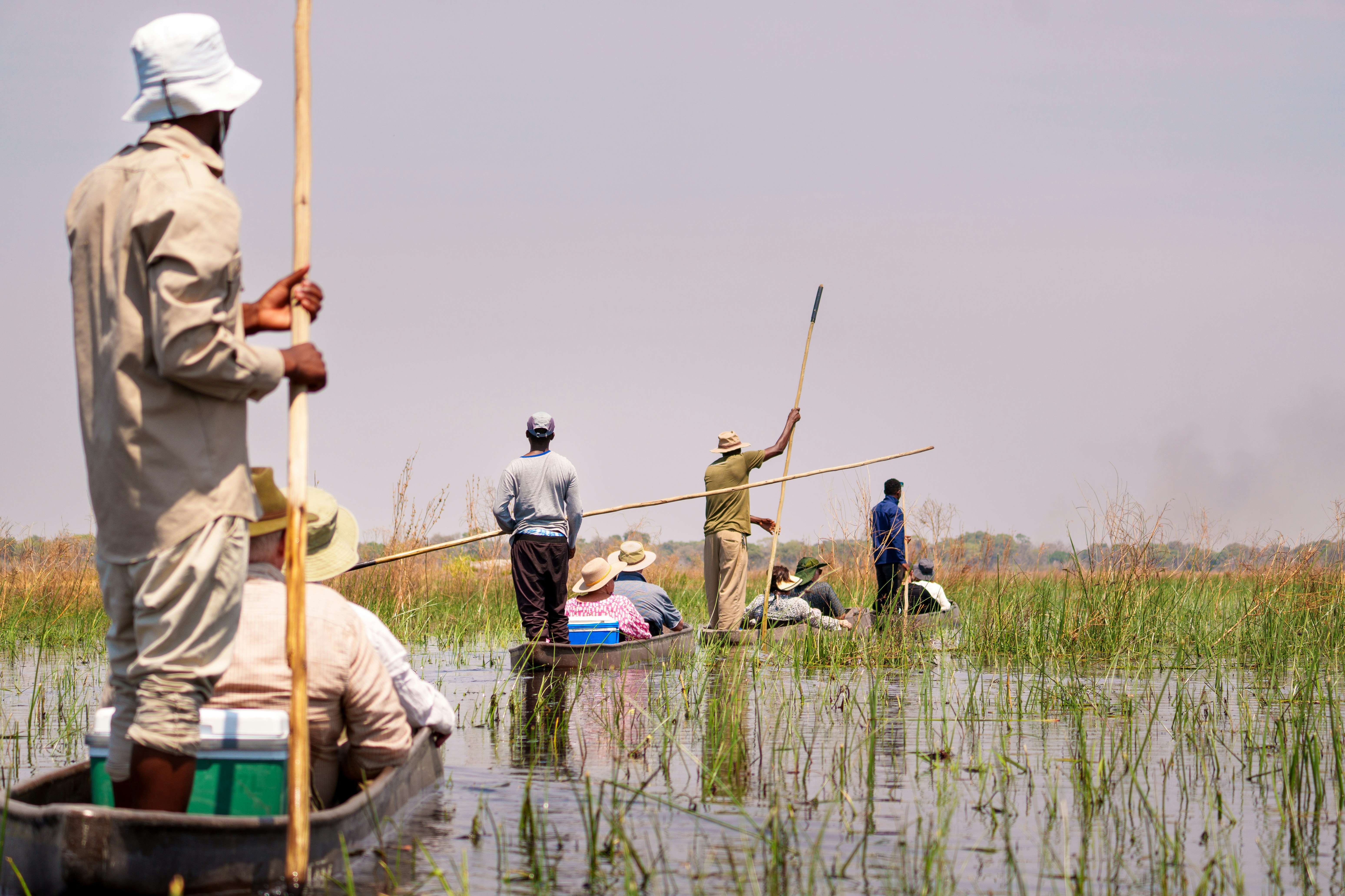 Local men carry passengers down a river on canoes.