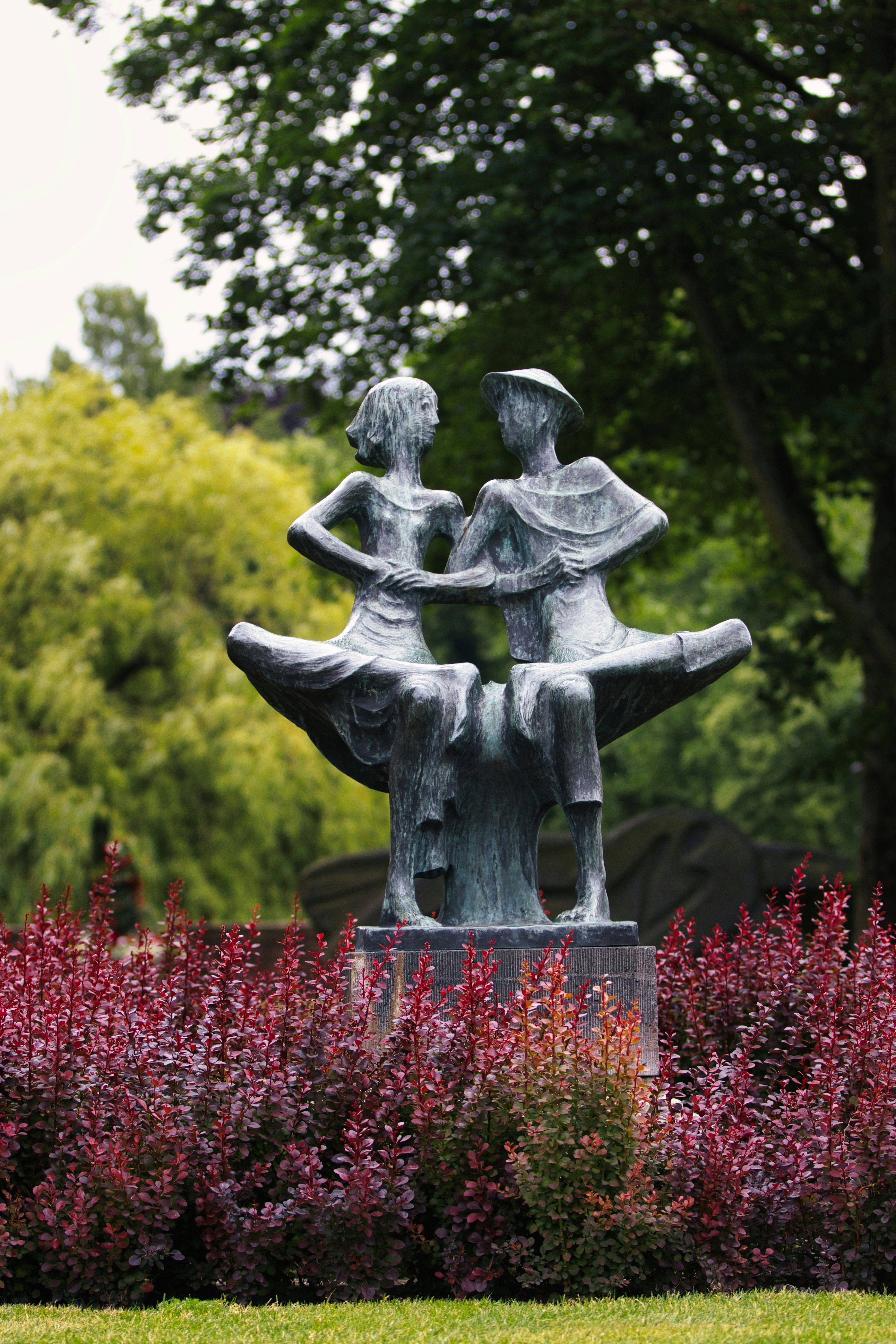 Sculpture of two figures sitting together in a garden.