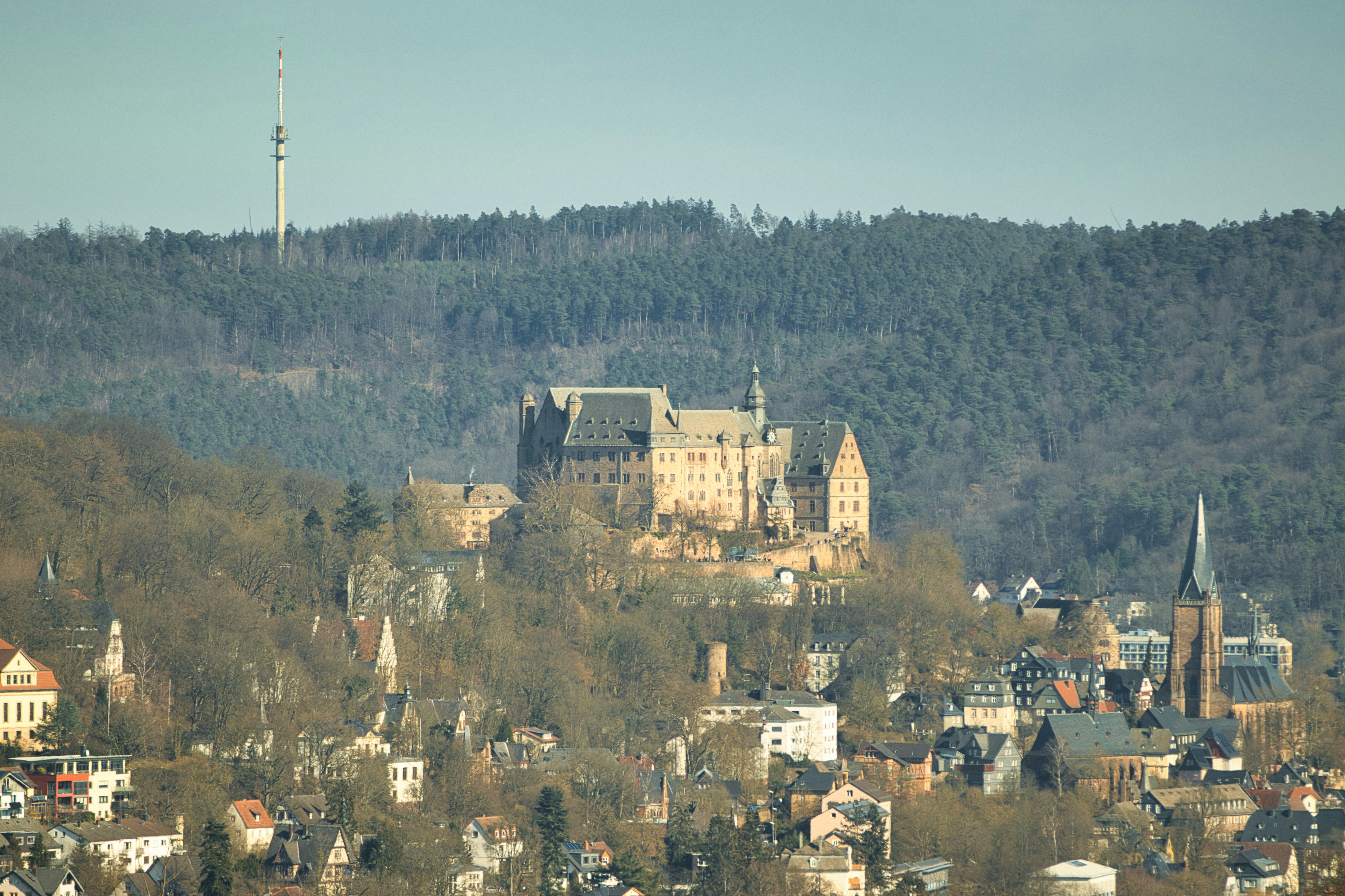 Castle overlooking a town with a distant tower.