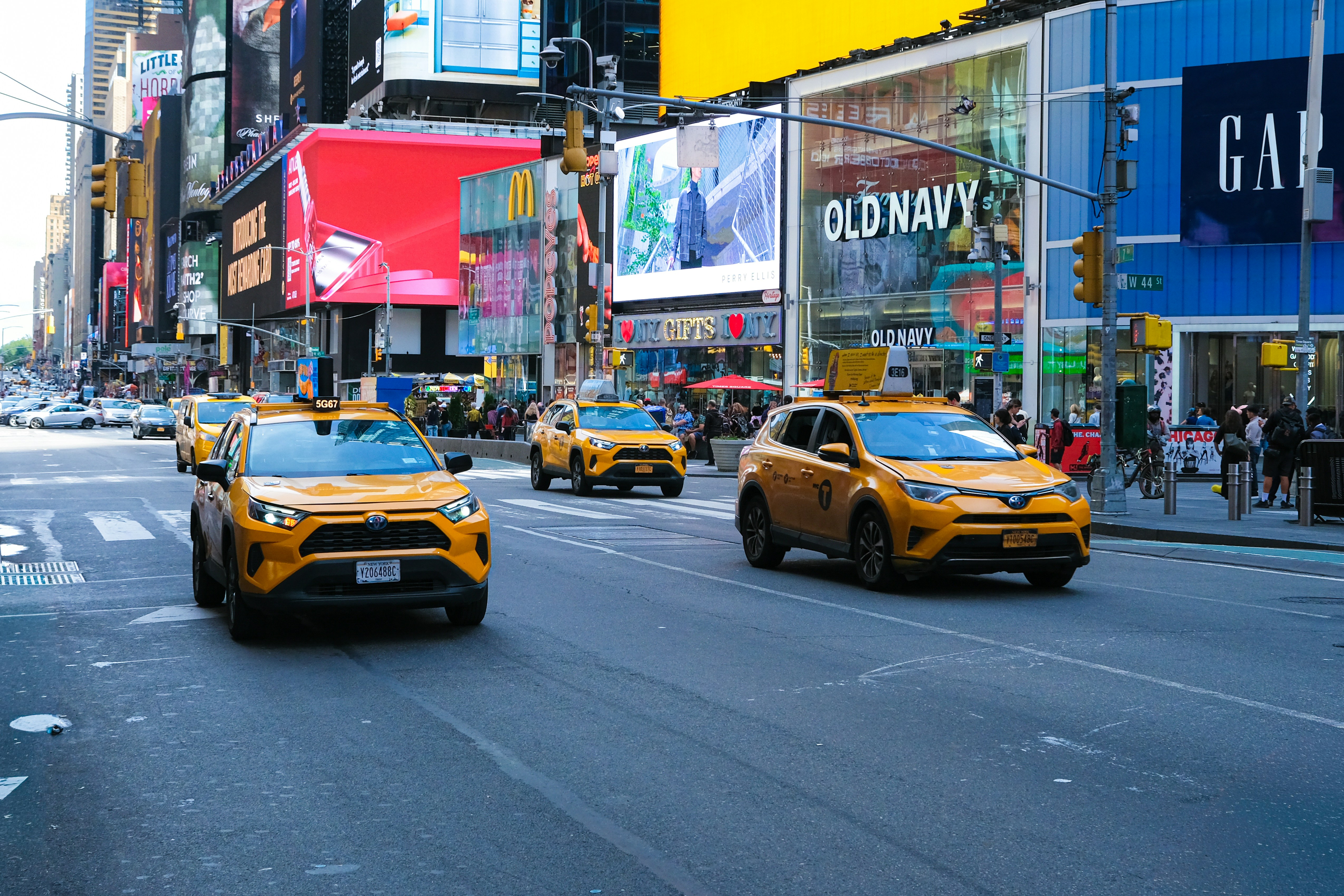 Yellow taxis drive down a busy city street with billboards.