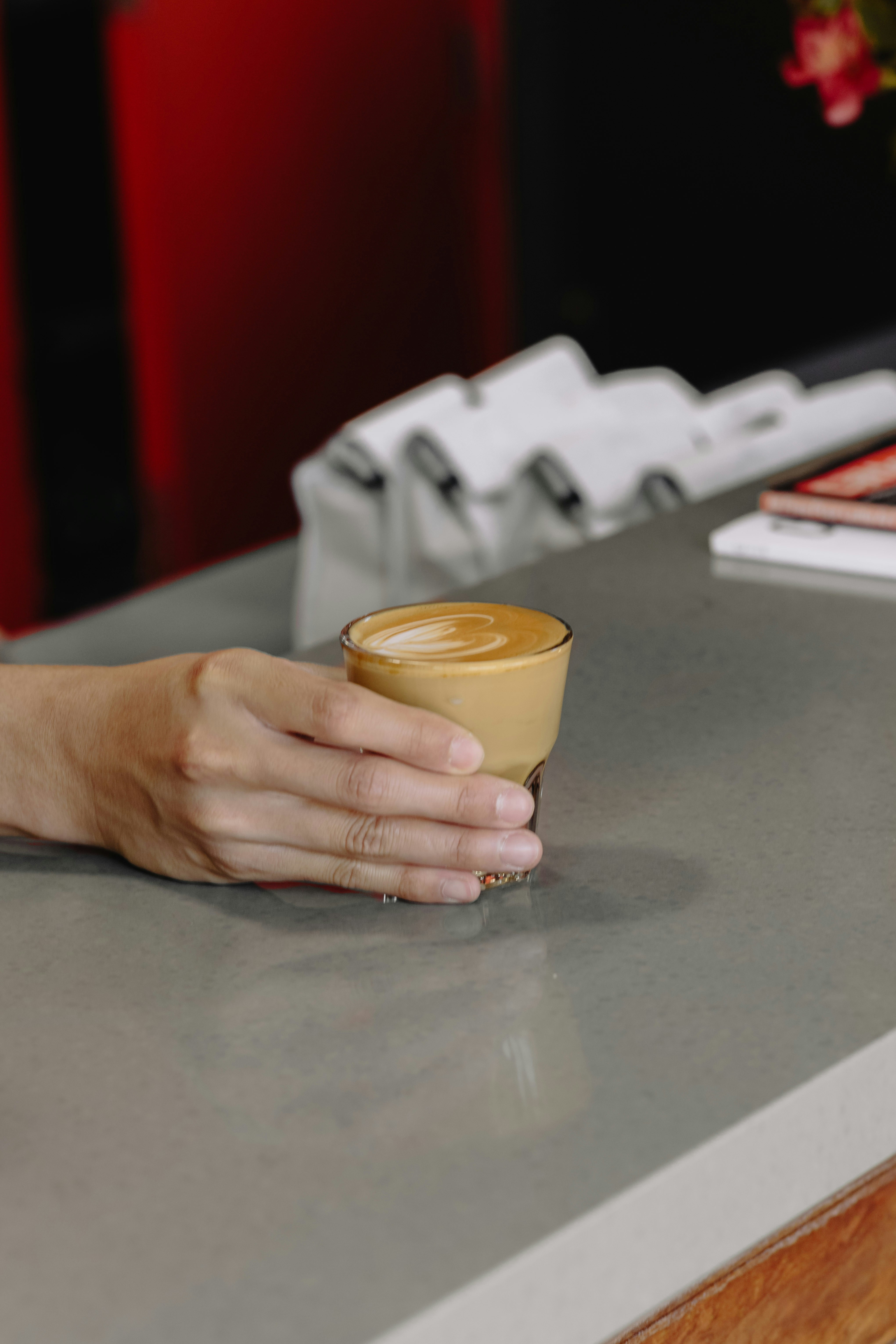Hand holding a glass of latte with foam art.