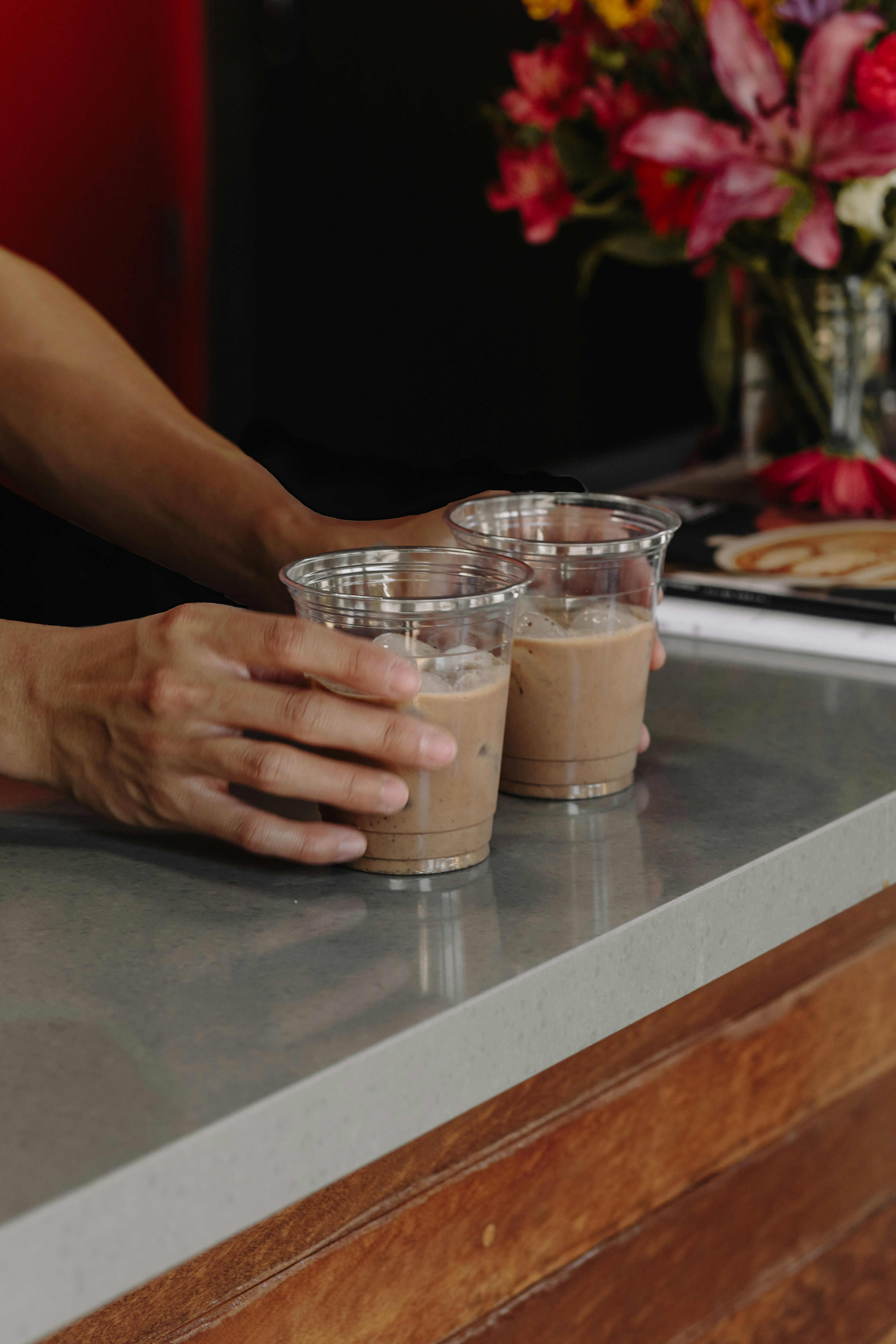 Tangan memegang dua minuman es kopi di meja