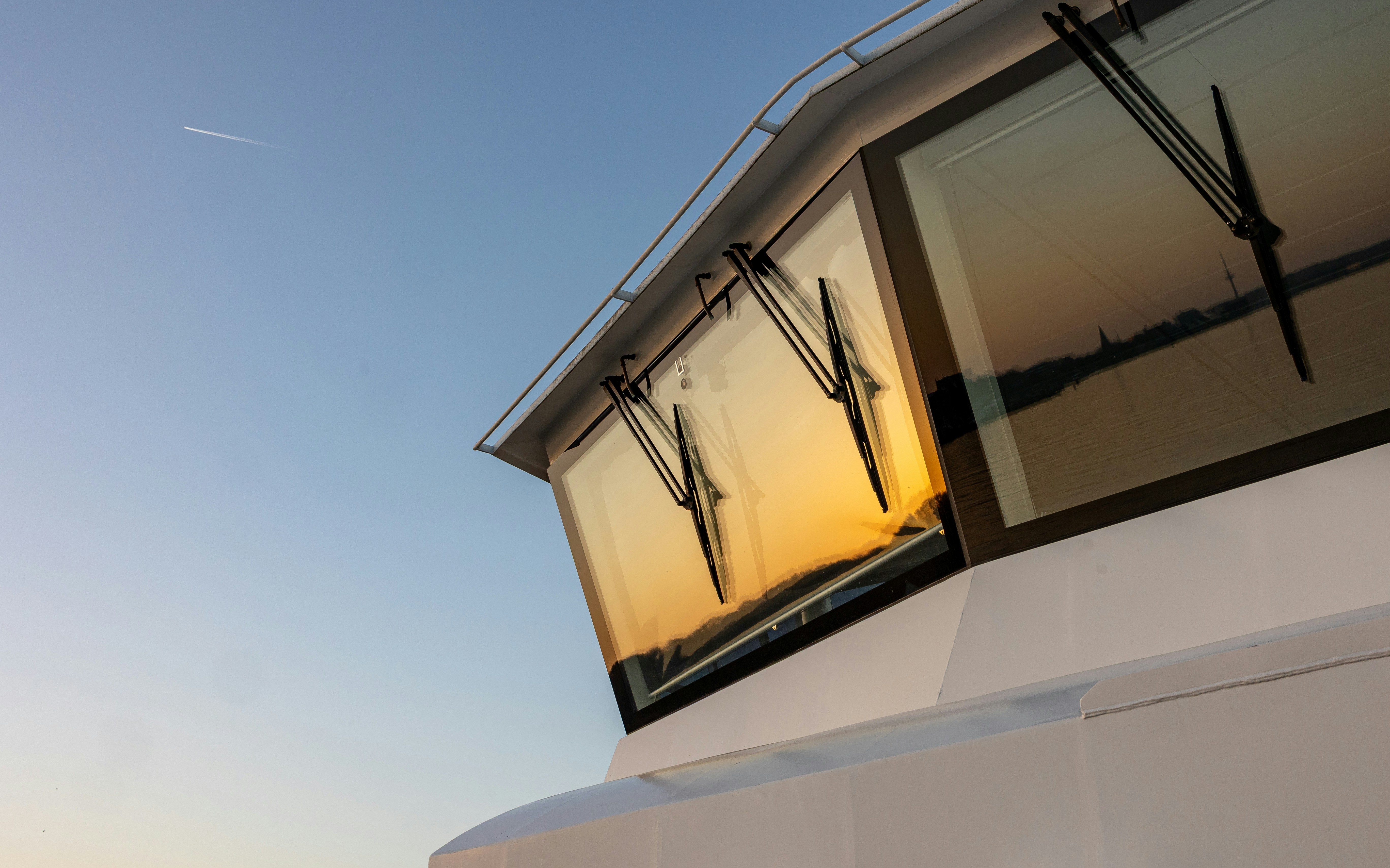 Ship's bridge windows reflect sunset over water.