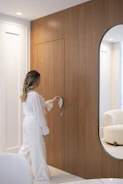 Woman in white reaching for a wooden door handle.