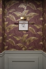 Framed artwork hangs on a wall with tropical leaf wallpaper.