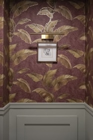 Framed artwork hangs on a wall with tropical leaf wallpaper.