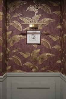 Framed artwork hangs on a wall with tropical leaf wallpaper.