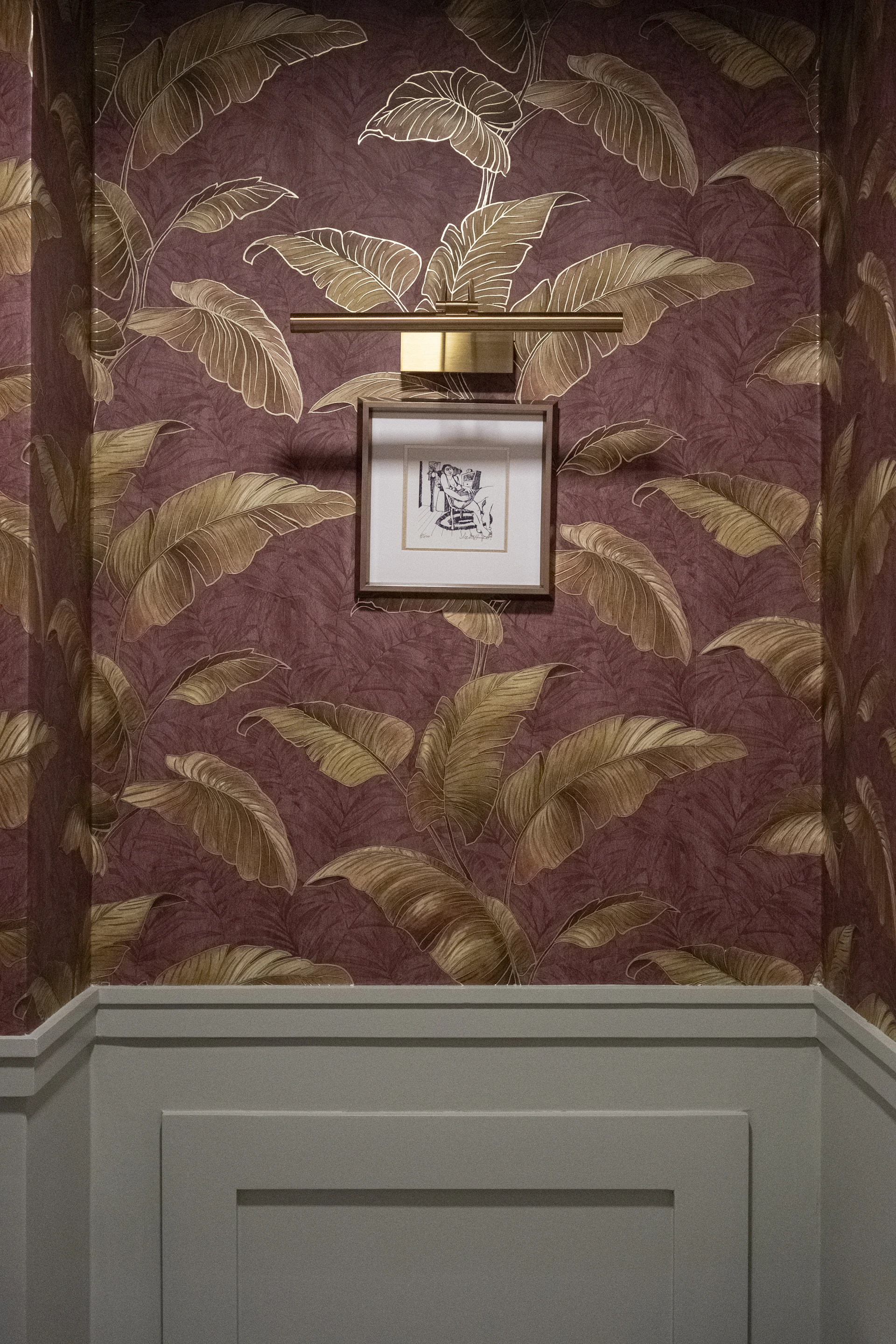 Framed artwork hangs on a wall with tropical leaf wallpaper.