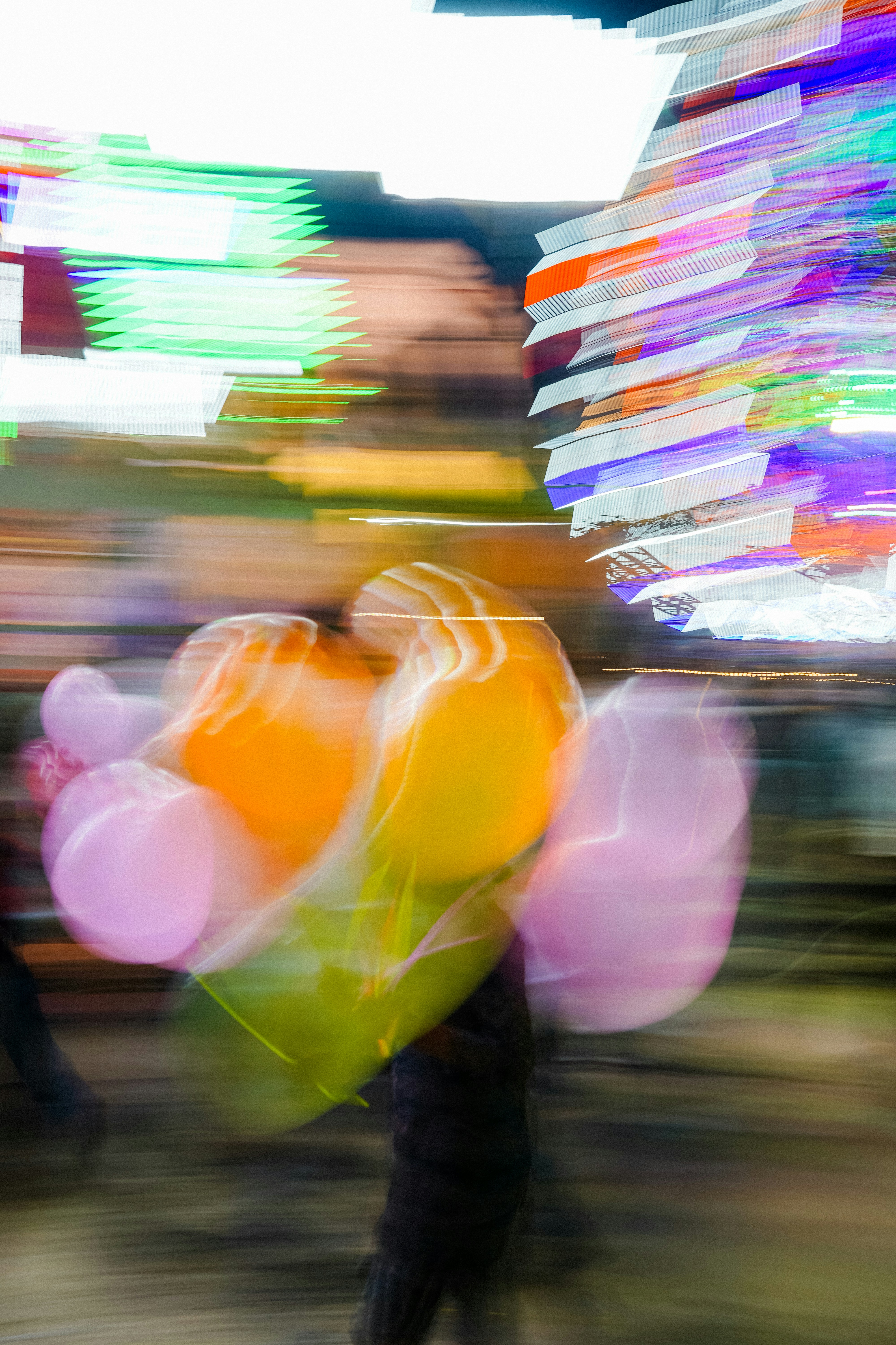 Persona borrosa sosteniendo globos de colores por la noche.