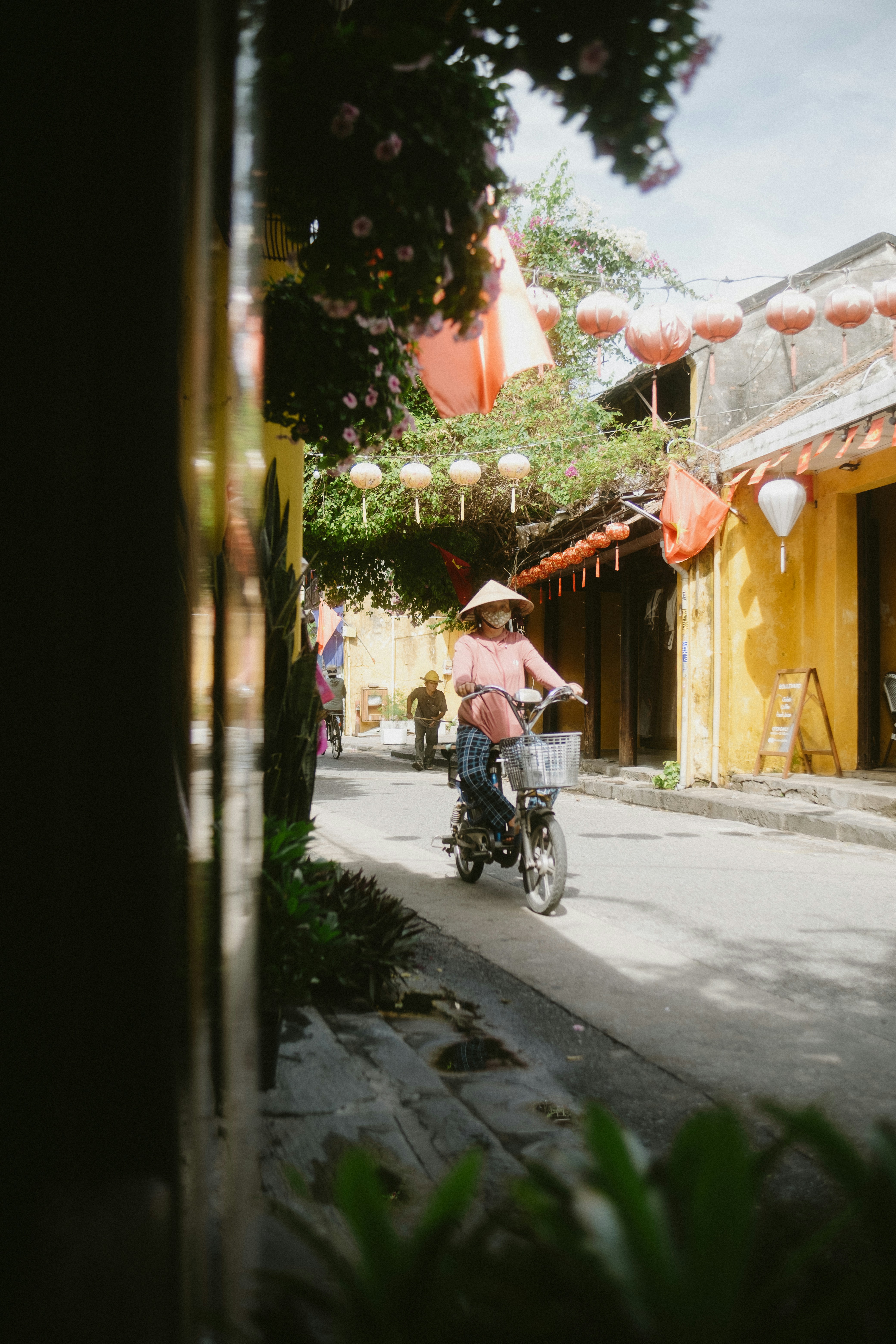 Woman in conical hat rides bicycle down sunny street