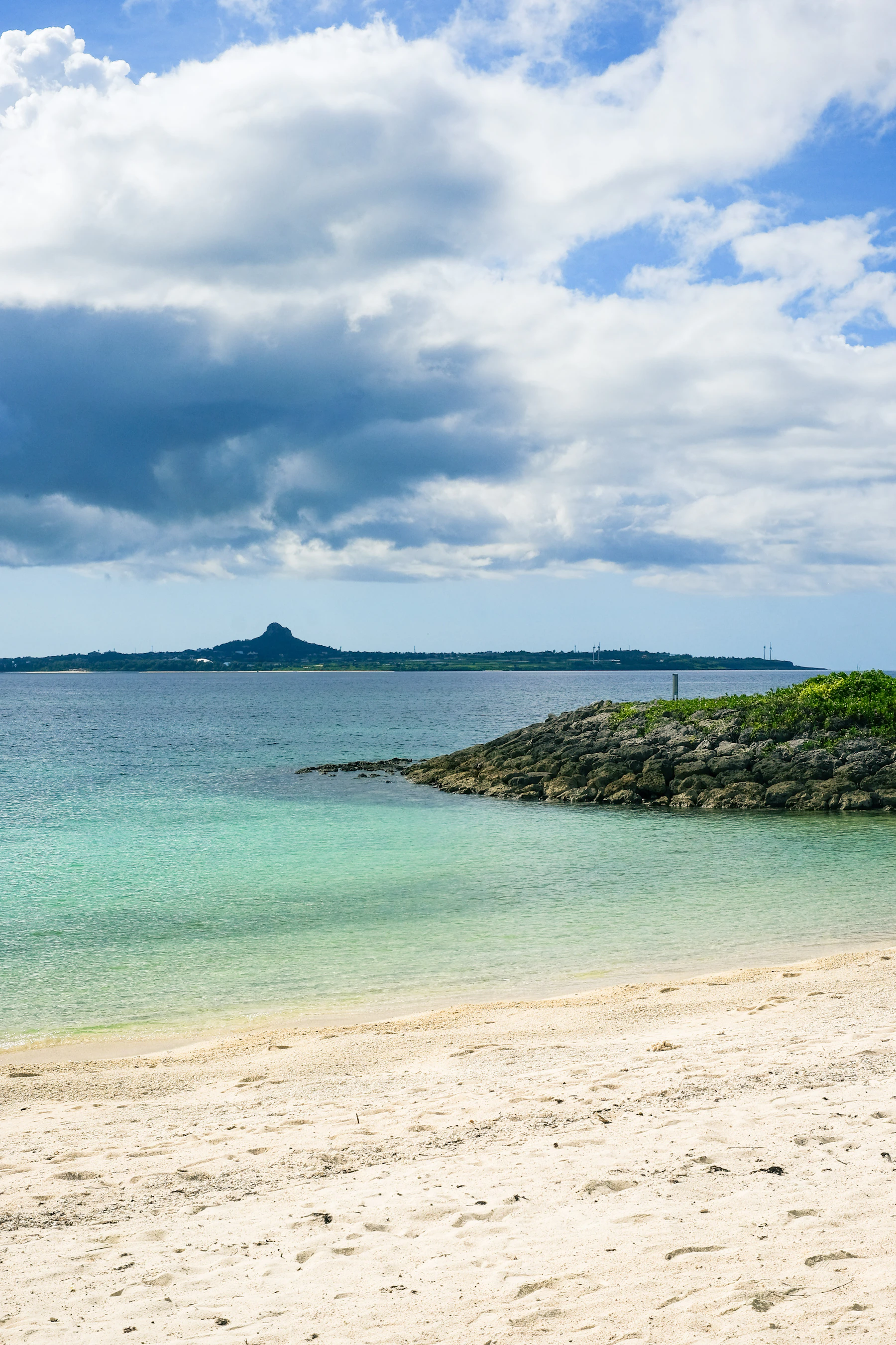 Heller Sandstrand und ruhige türkisfarbene Bucht mit Inselblick auf Okinawa