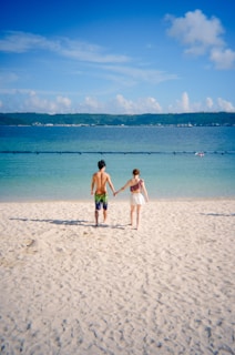 Couple holding hands walking on a sandy beach.