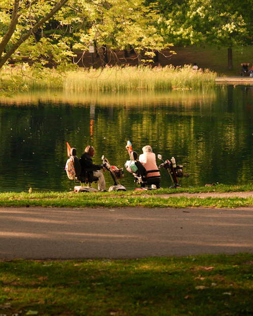 Two people on scooters by a lake.
