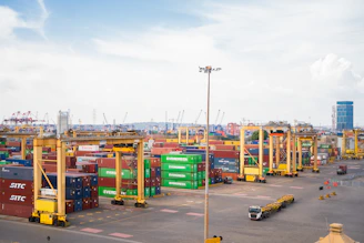 Shipping containers stacked at a busy port with cranes.