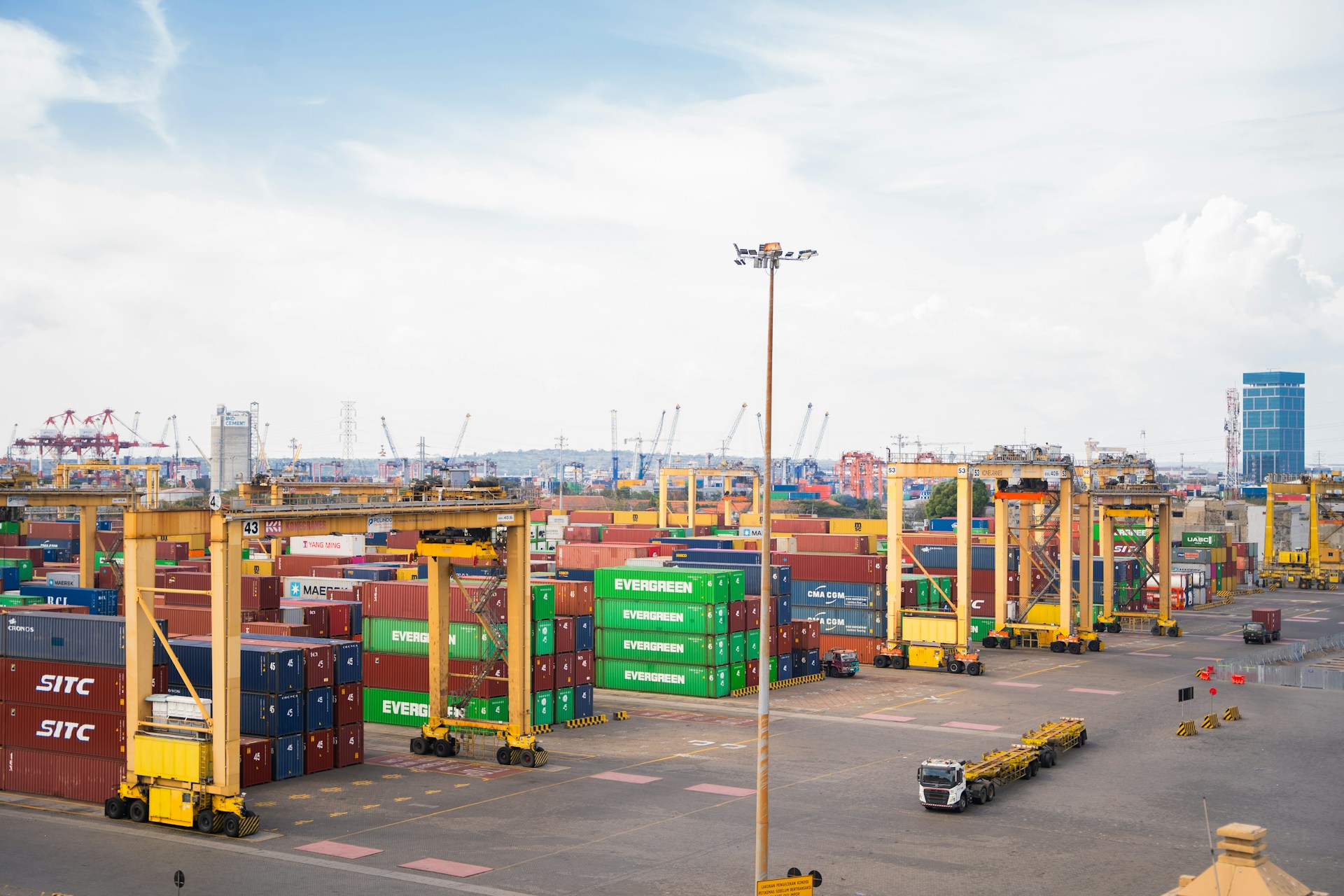 Shipping containers stacked at a busy port with cranes.