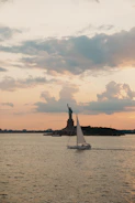Sailboat passes statue of liberty at sunset