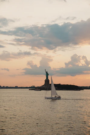 Sailboat passes statue of liberty at sunset
