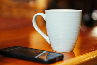 White mug and smartphone on wooden table