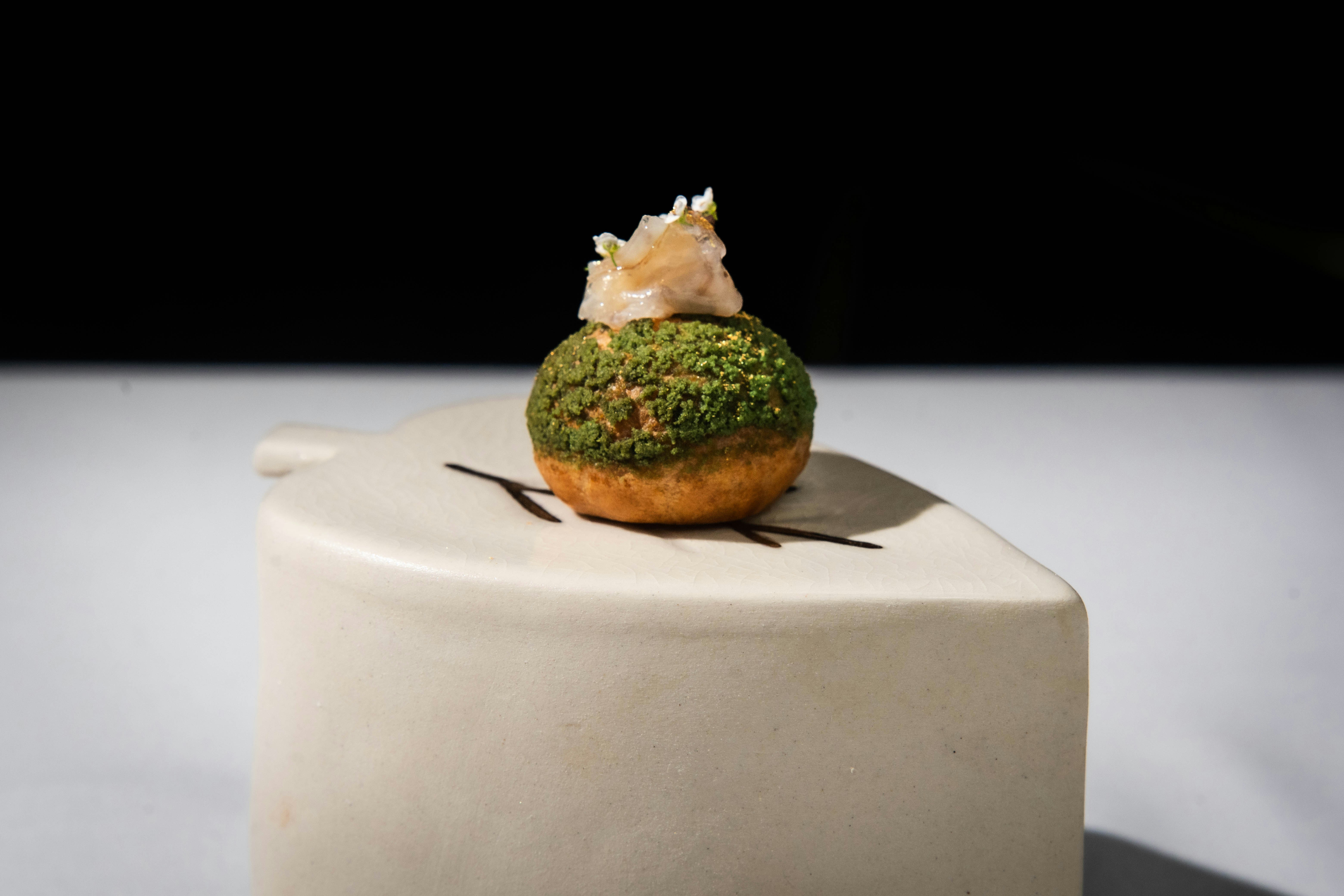 A small green pastry with white topping on a stand