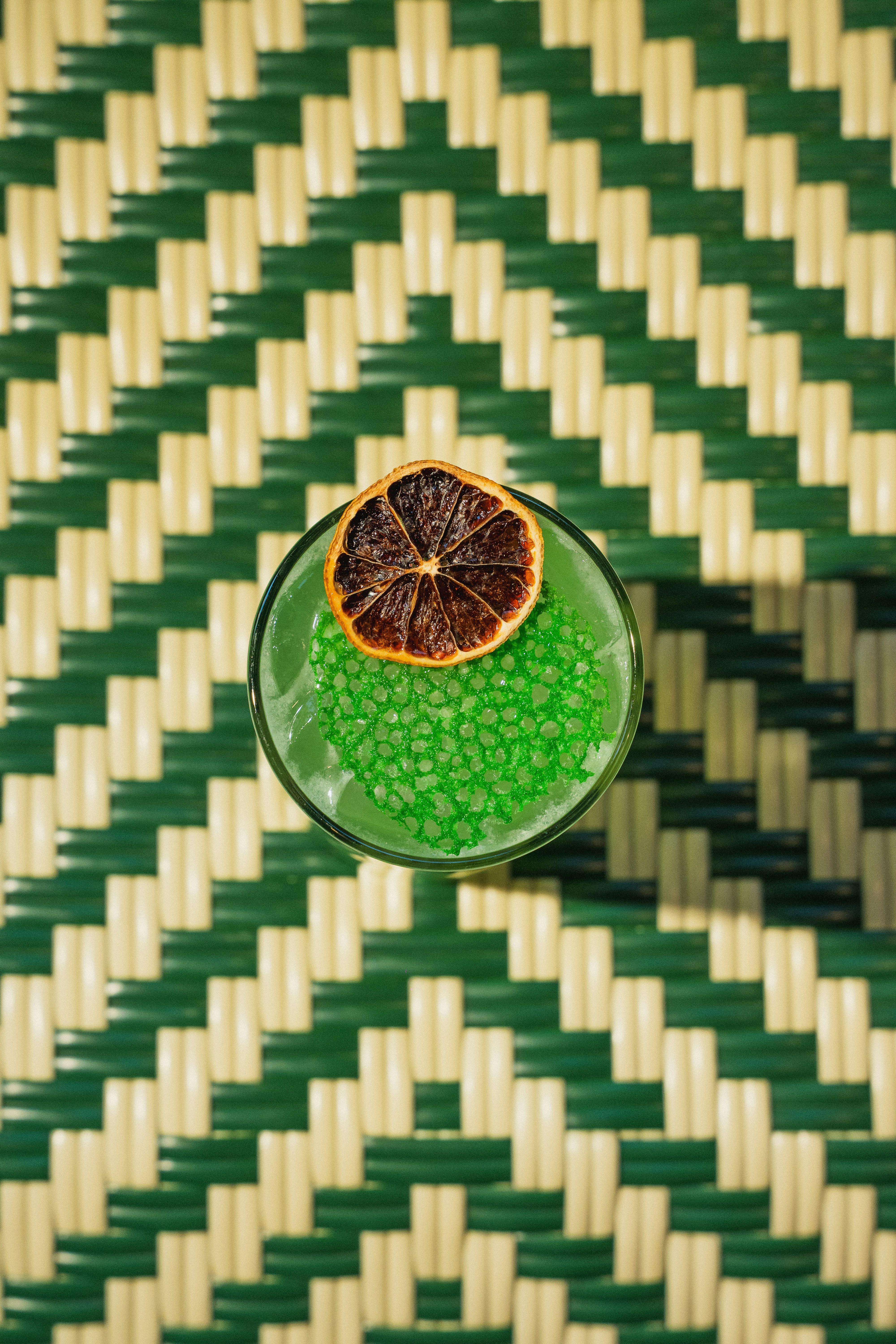 Cóctel verde con rodaja de naranja seca sobre fondo tejido